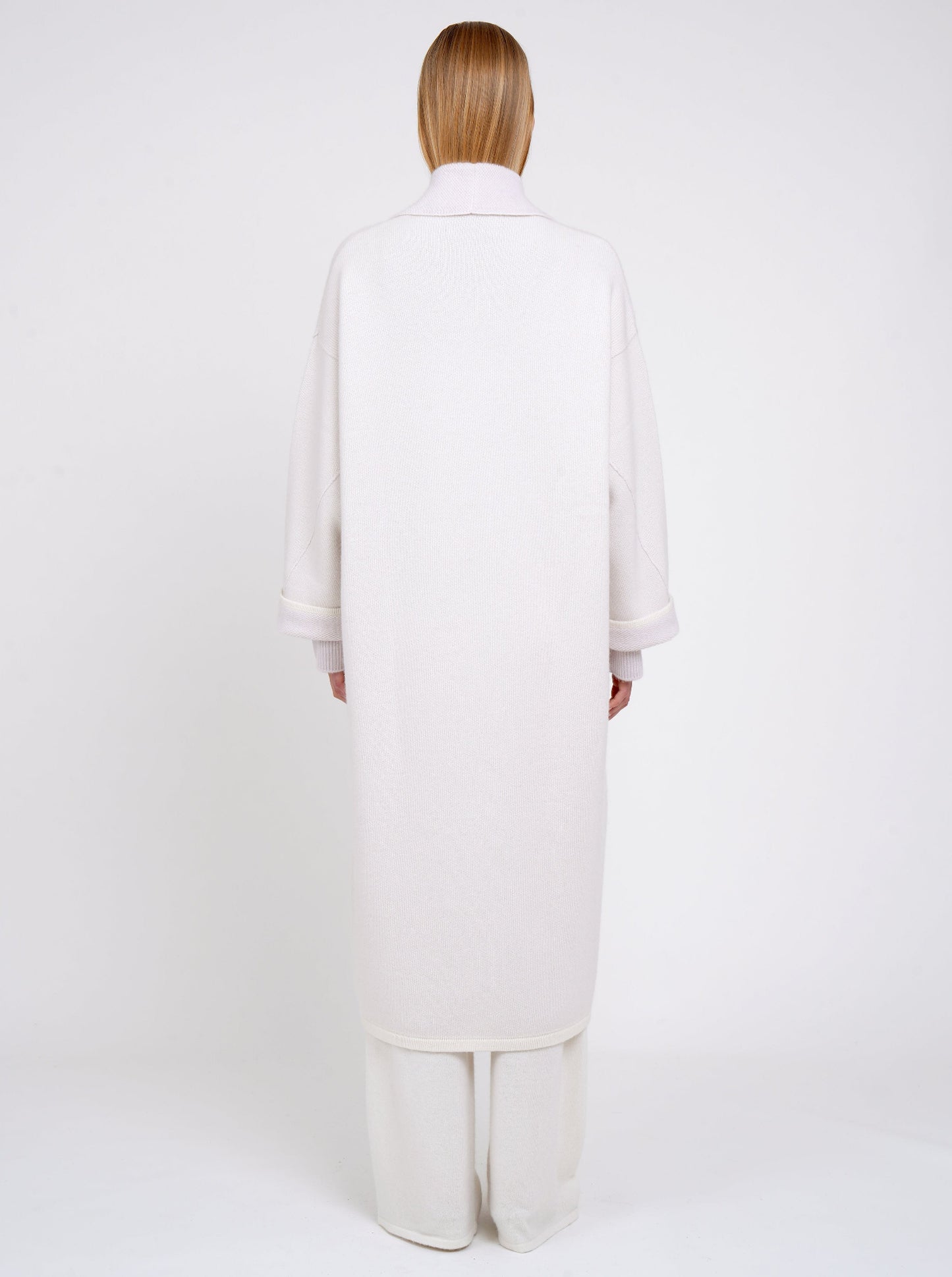 Back view model in lilac and white mix cashmere knit long coat with lilac collar revere and turn back cuffs; with wide leg white cashmere pants.