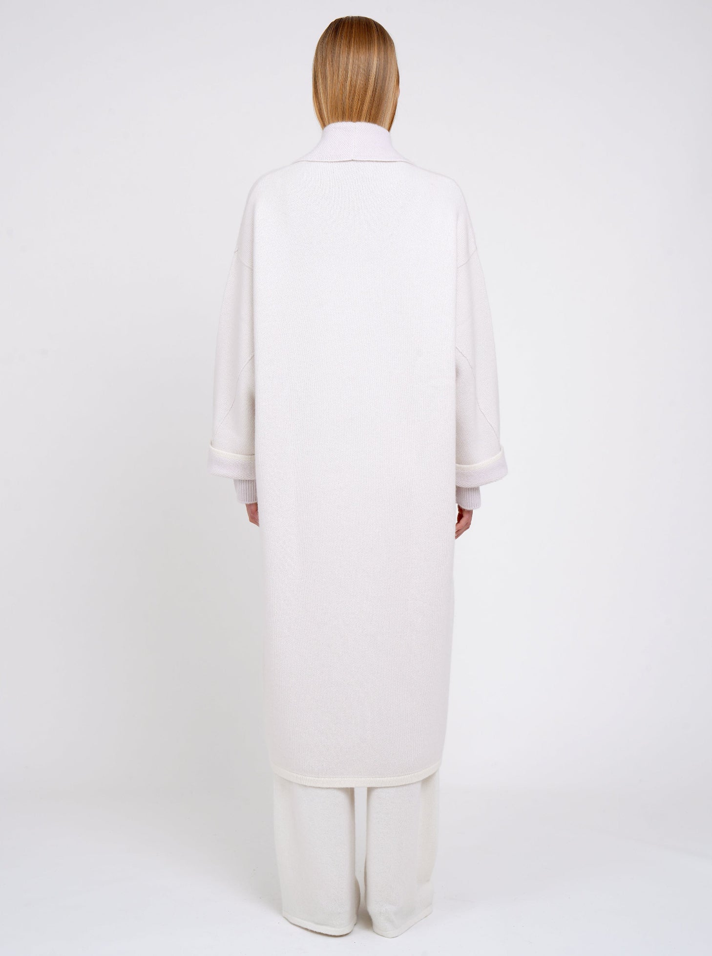 Back view model in lilac and white mix cashmere knit long coat with lilac collar revere and turn back cuffs; with wide leg white cashmere pants.