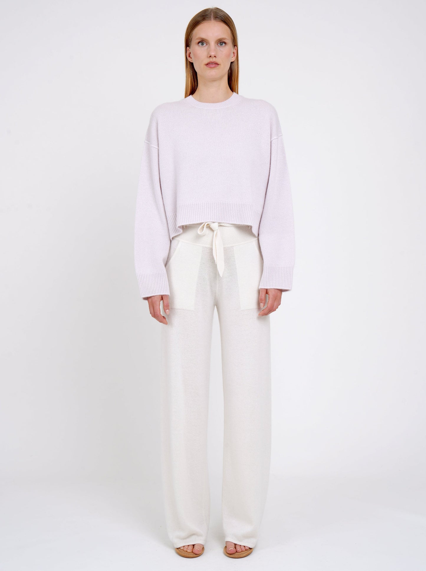 Model wears lilac cashmere cropped jumper with round neck, long sleeves; worn with white cashmere, wide leg, belted pants.