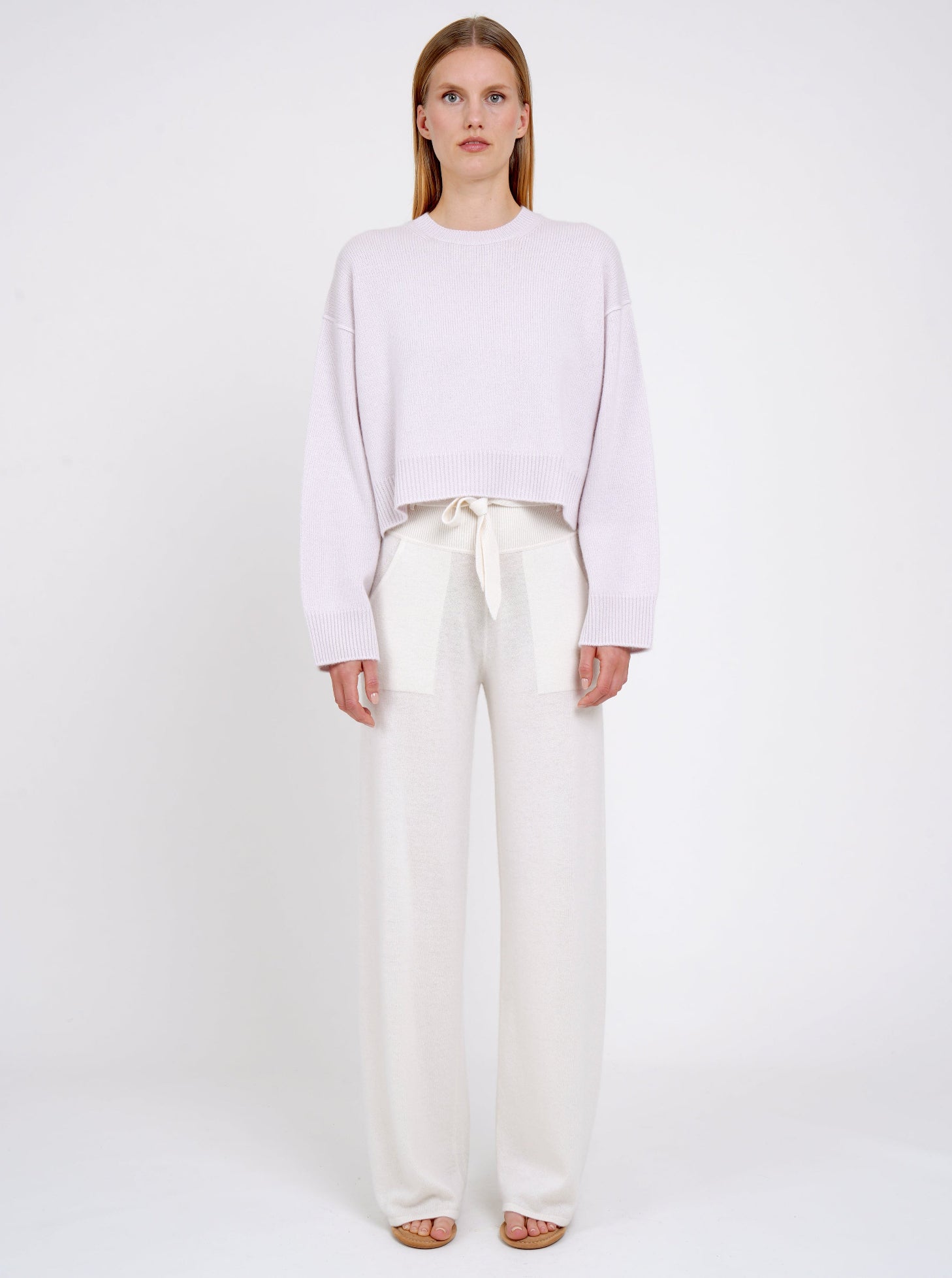 Model wears lilac cashmere cropped jumper with round neck, long sleeves; worn with white cashmere, wide leg, belted pants.