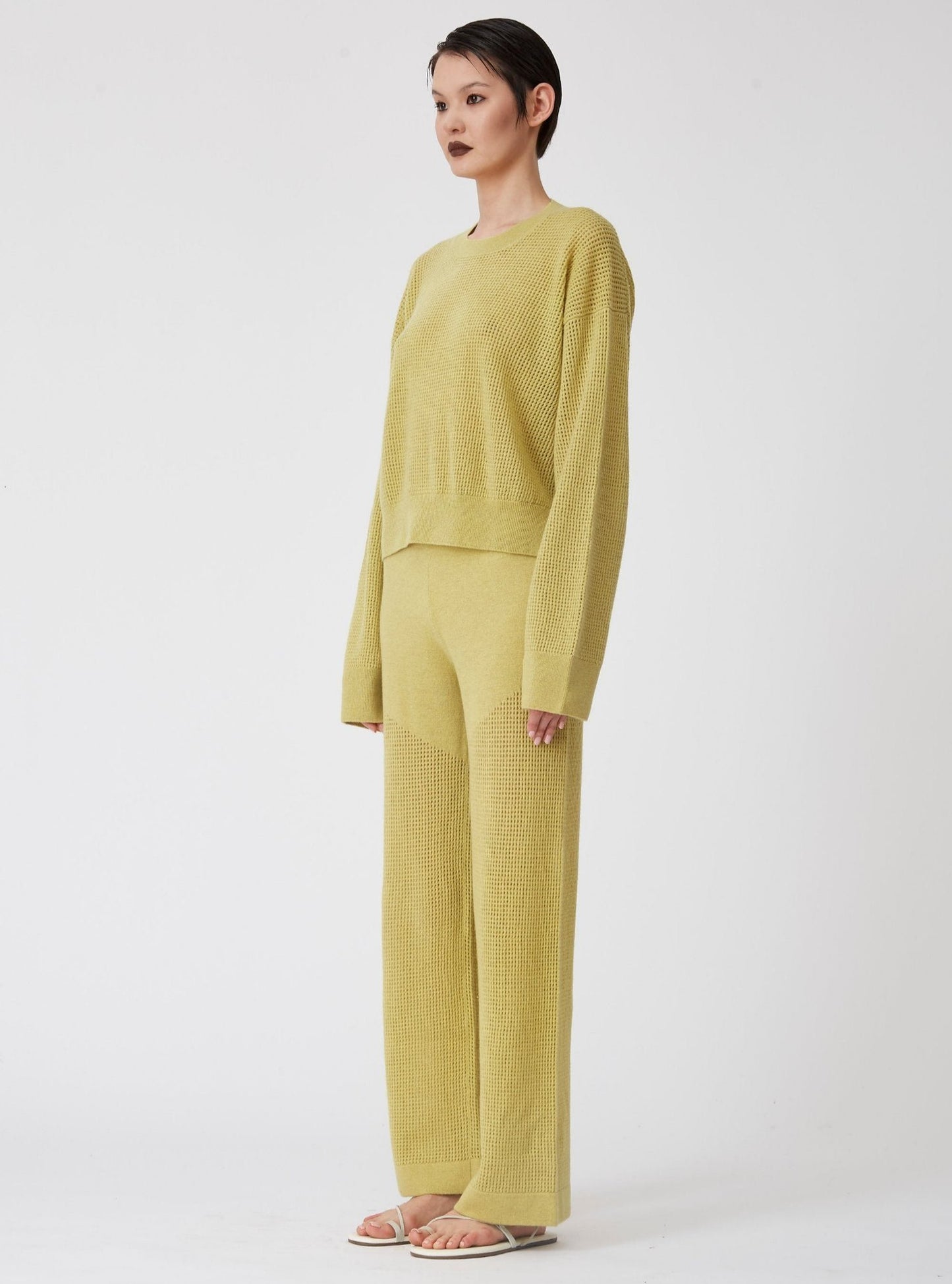 Side view of model wearing lime green light-weight net knit cashmere long sleeve sweater with wide leg matching pants.