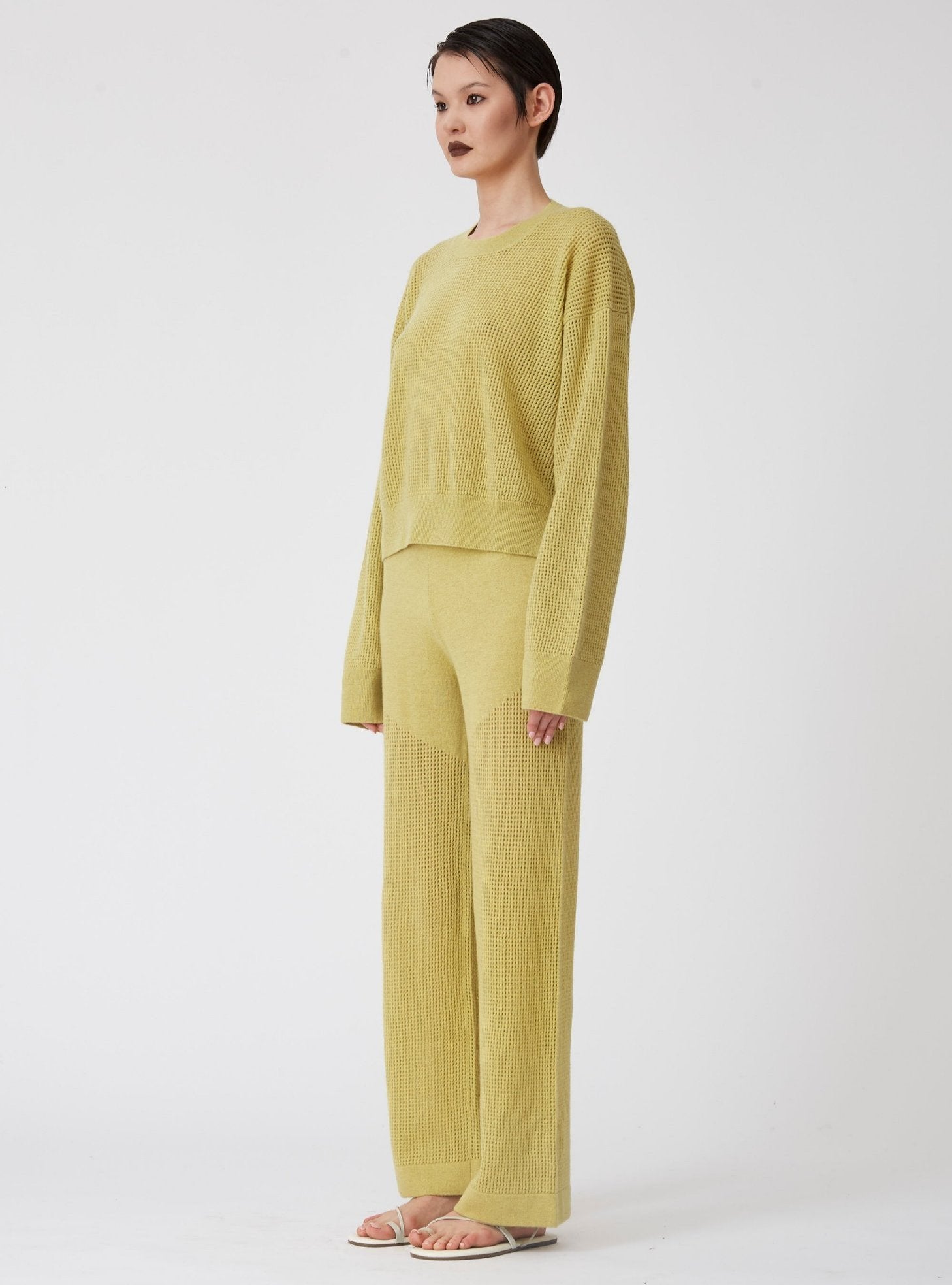 Side view of model wearing lime green light-weight net knit cashmere long sleeve sweater with wide leg matching pants.