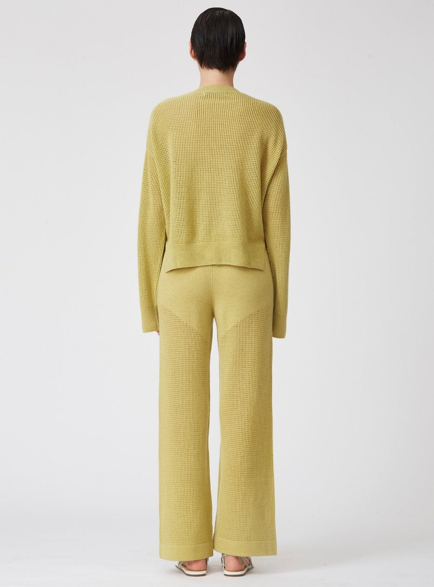 Back view of model wearing lime green cashmere net knit long sleeve sweater with matching lime green net knit wide leg pants.