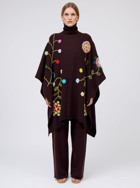 Front view model wearing mahogany brown cashmere mid-length wrap with brightly coloured hand-embroidery; worn with matching brown jumper and brown pants.