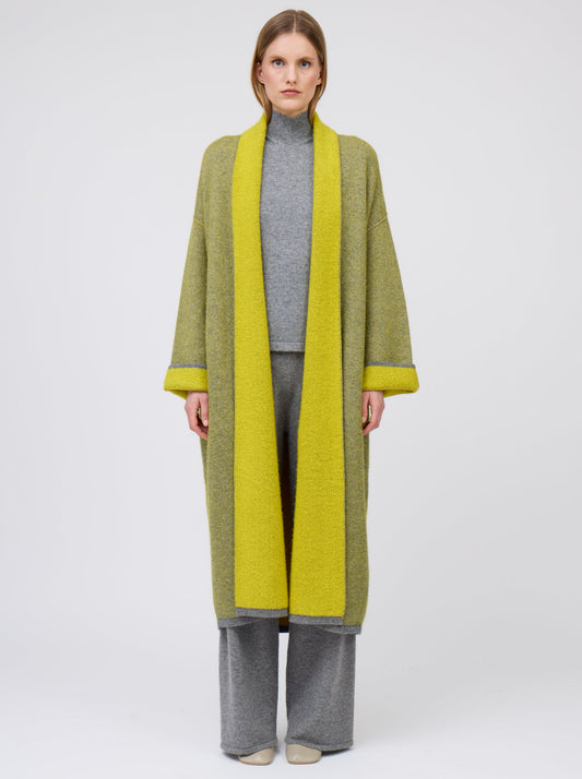 Front straight view model in long mustard yellow and grey mix cashmere knit coat with yellow collar revere and turn back cuffs; wearing with grey knit top and wide leg cashmere pants.