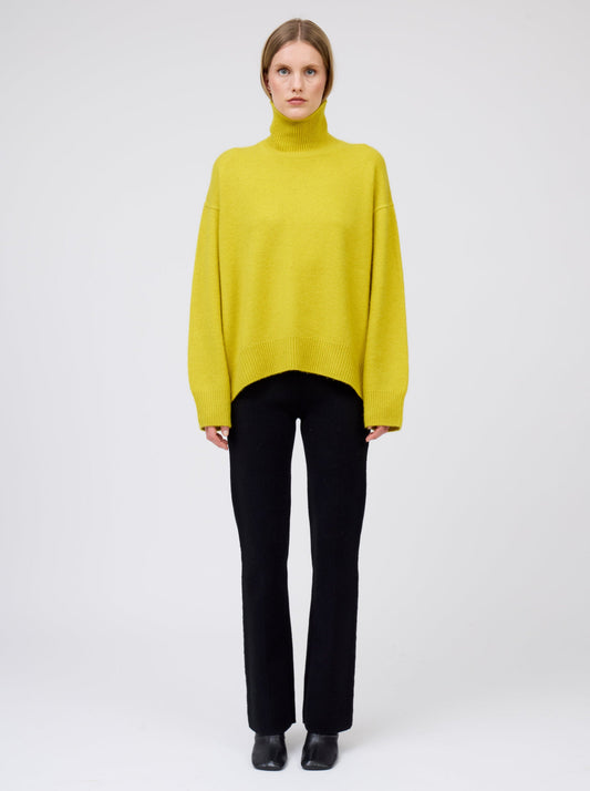 Straight on front view model wears mustard yellow cashmere roll neck oversized jumper with black tailored cashmere pants.