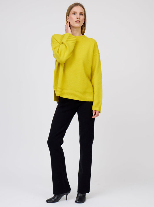 Relaxed standing pose model wearing mustard yellow oversized round neck sweater with black suit pants and black boots.