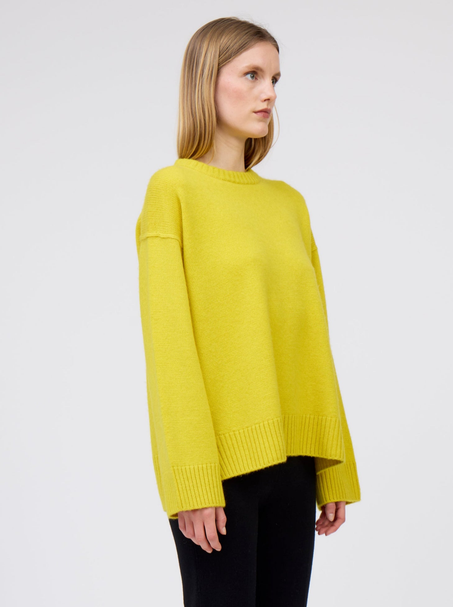 Cropped close up of model in mustard yellow oversized round neck sweater with long sleeves and black suit trousers. 