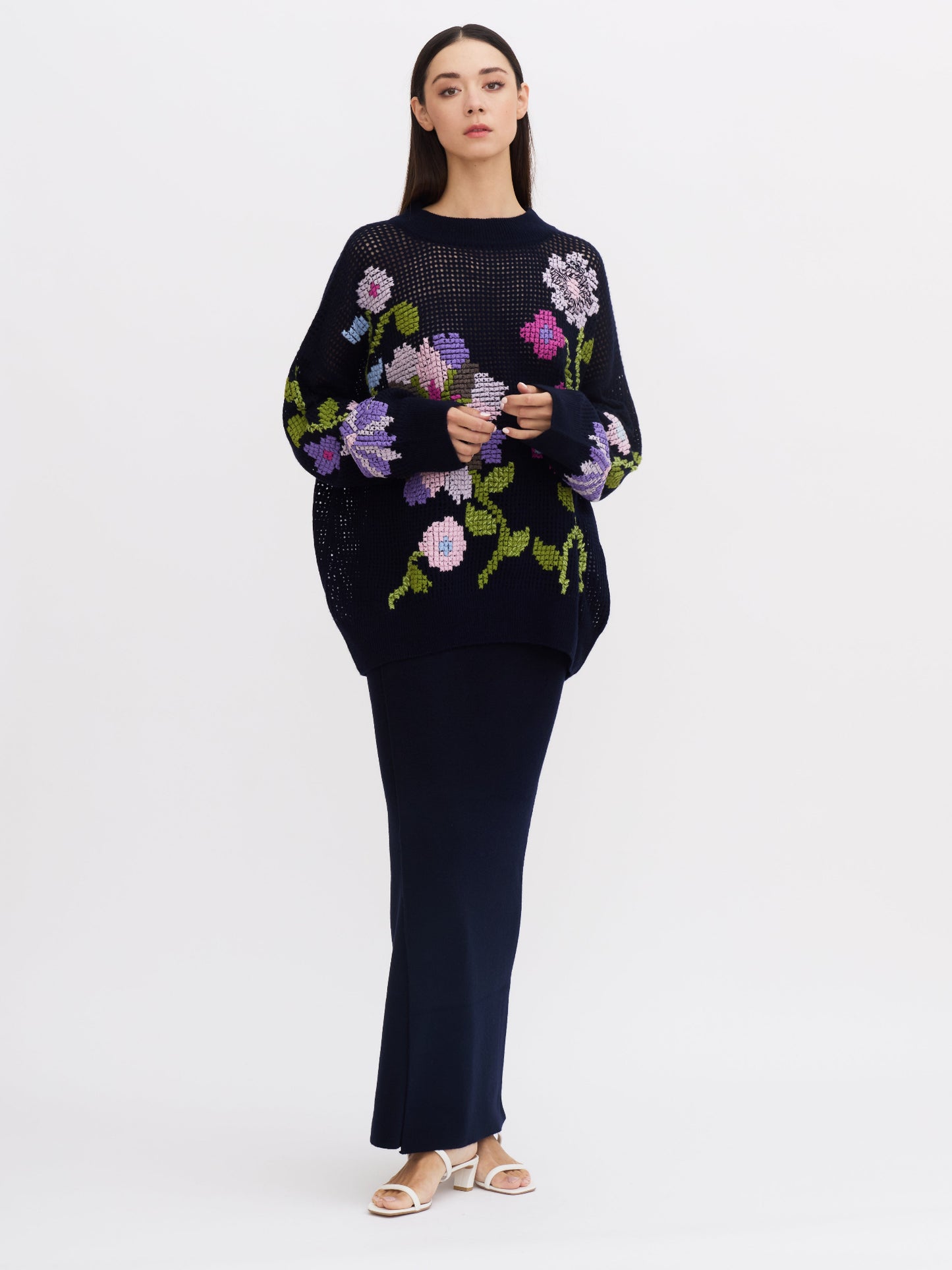 Front view of model wearing women's navy cashmere slim, dark  navy maxi-length wrap skirt with navy, over-size floral cross-stitch jumper.