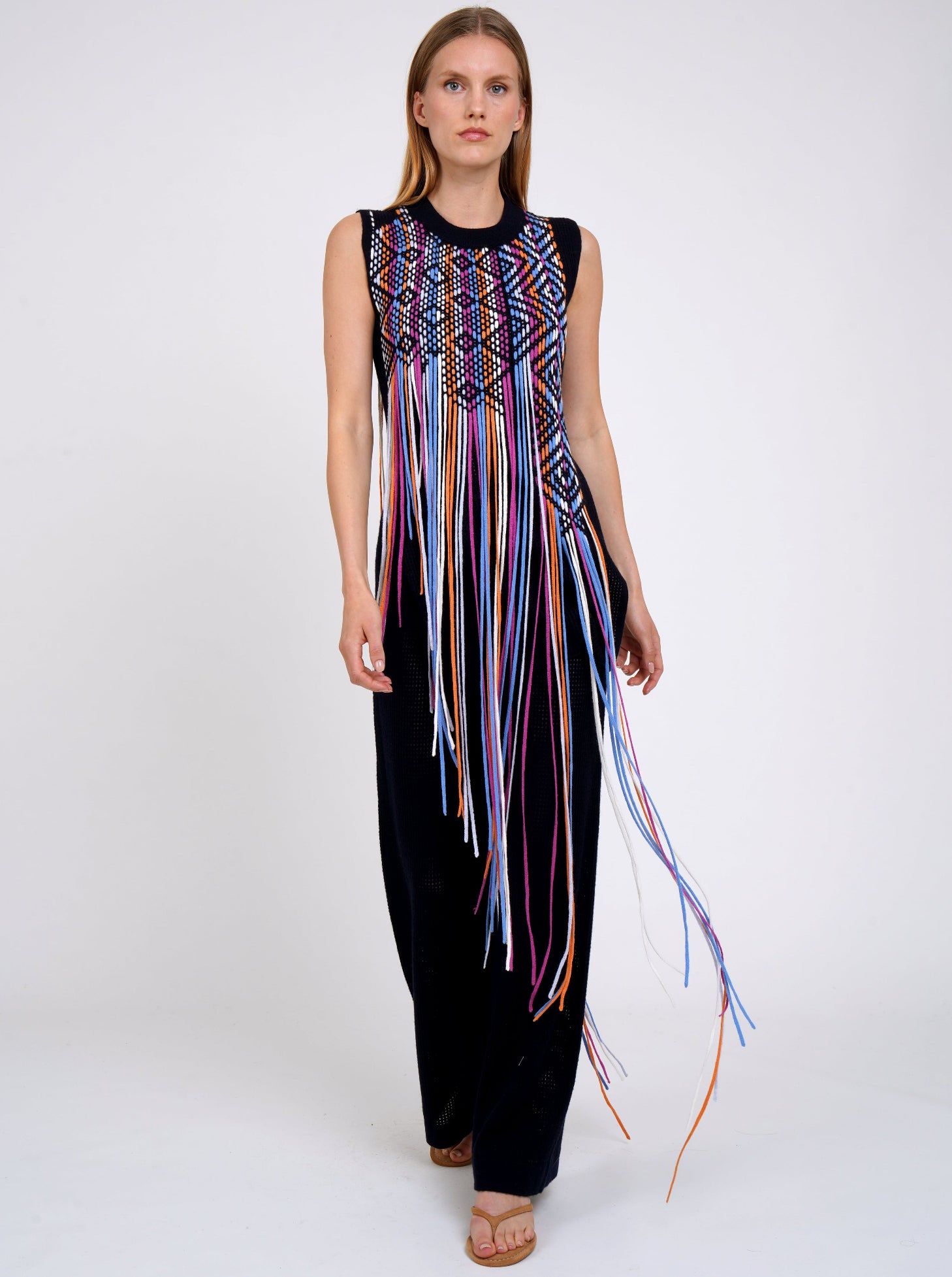 model walks towards camera wearing Navy light weight cashmere sleeveless tunic decorated with woven coloured long fringes worn with navy knit wide leg pants.