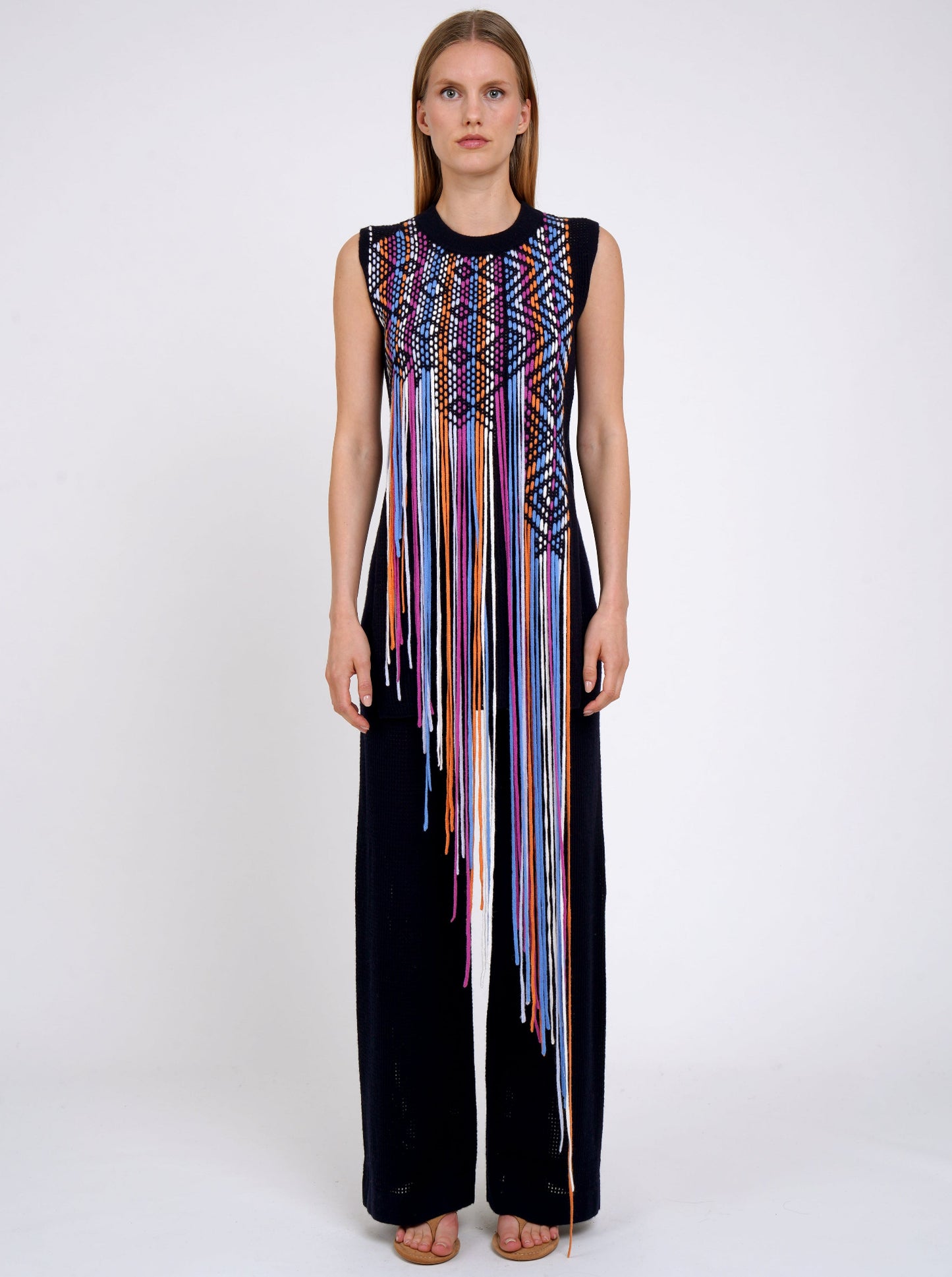 Front view model in navy light weight cashmere sleeveless tunic decorated with woven coloured long asymmetric fringes worn with navy knit wide leg pants.
