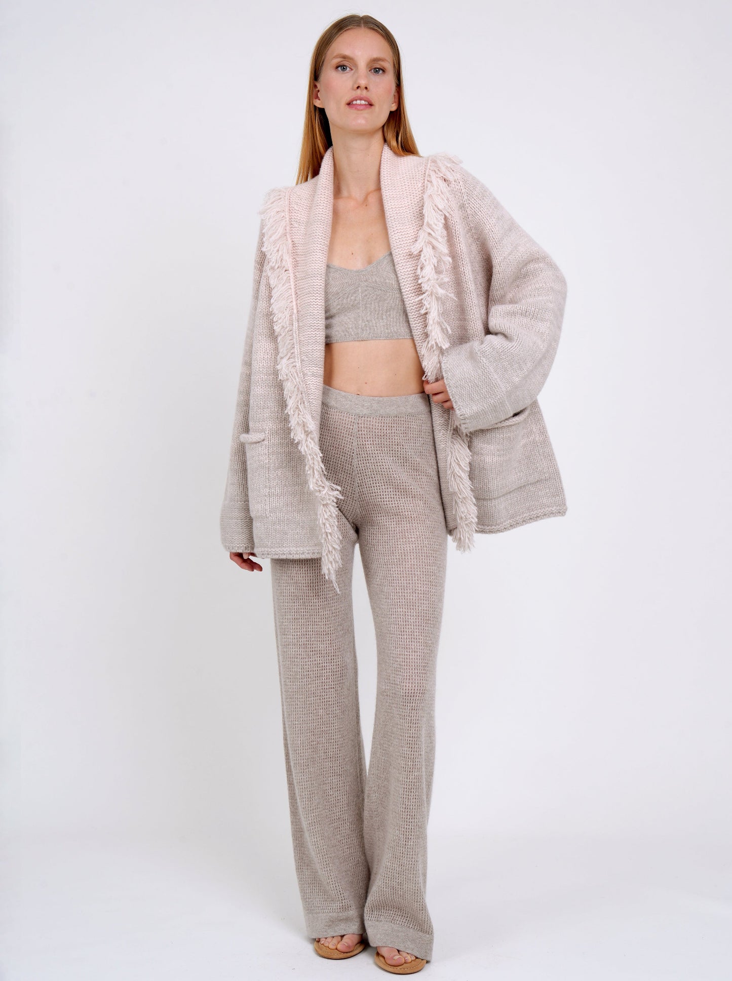 Model wears beige knit cropped bra top under beige chunky knit jacket with beige cashmere knit pants.