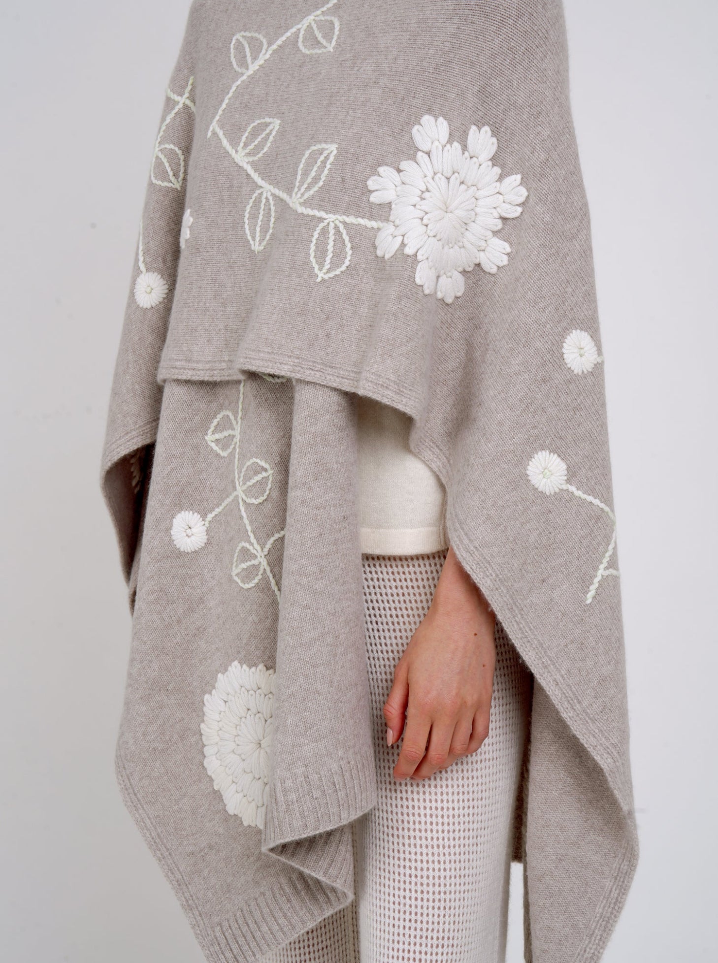 close up detail beige cashmere long shawl with large white embroidered flowers and white knit pants.