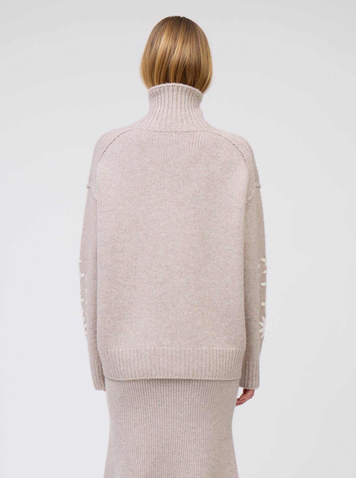 Back view model in chunky knit beige sweater with high turtle neck and beige knit flared skirt.