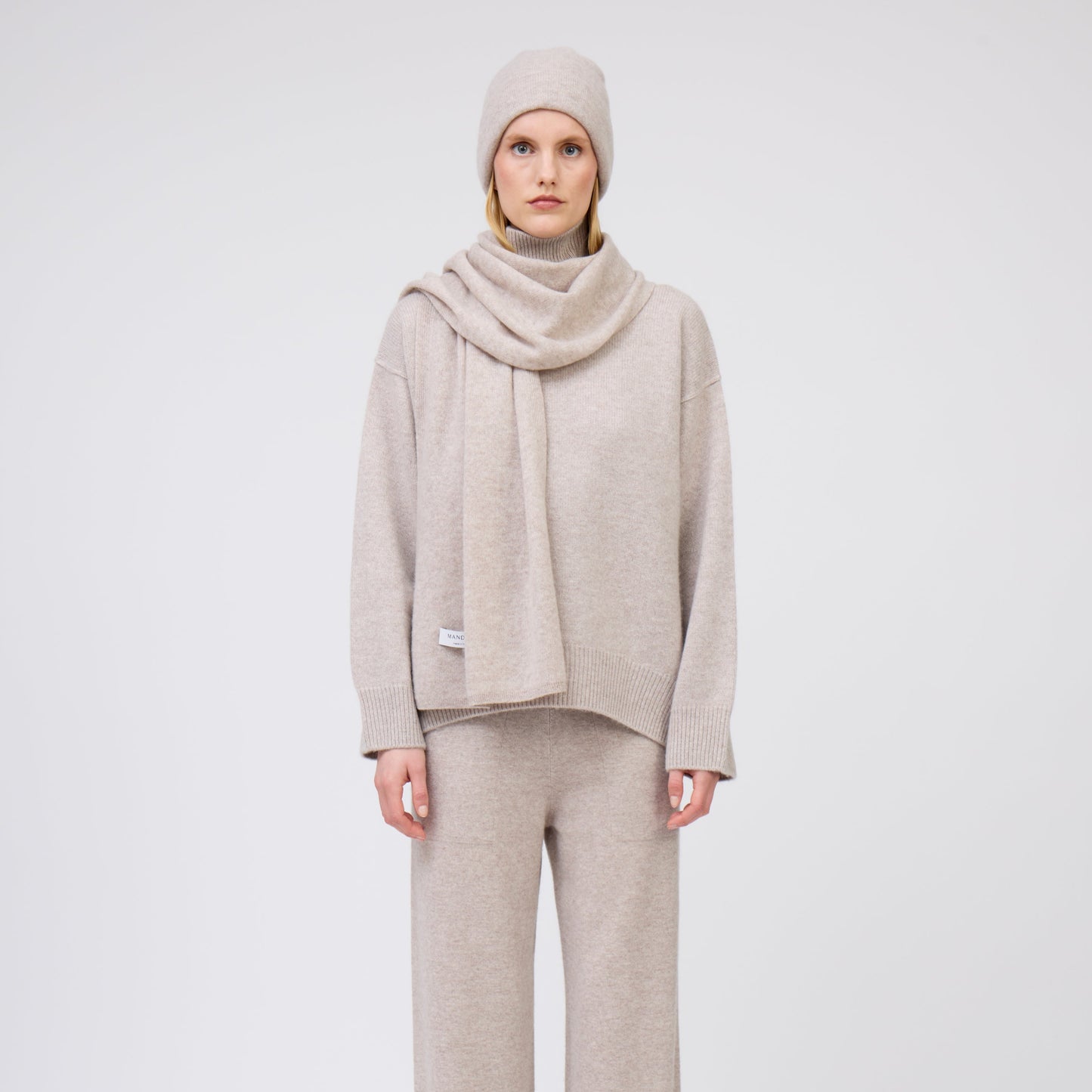 Front view of model wearing complete outfit in matching beige cashmere: beanie hat and scarf, jumper and pants.