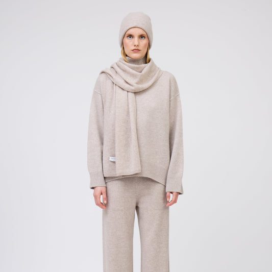 Front view of model wearing complete outfit in matching beige cashmere: beanie hat and scarf, jumper and pants.