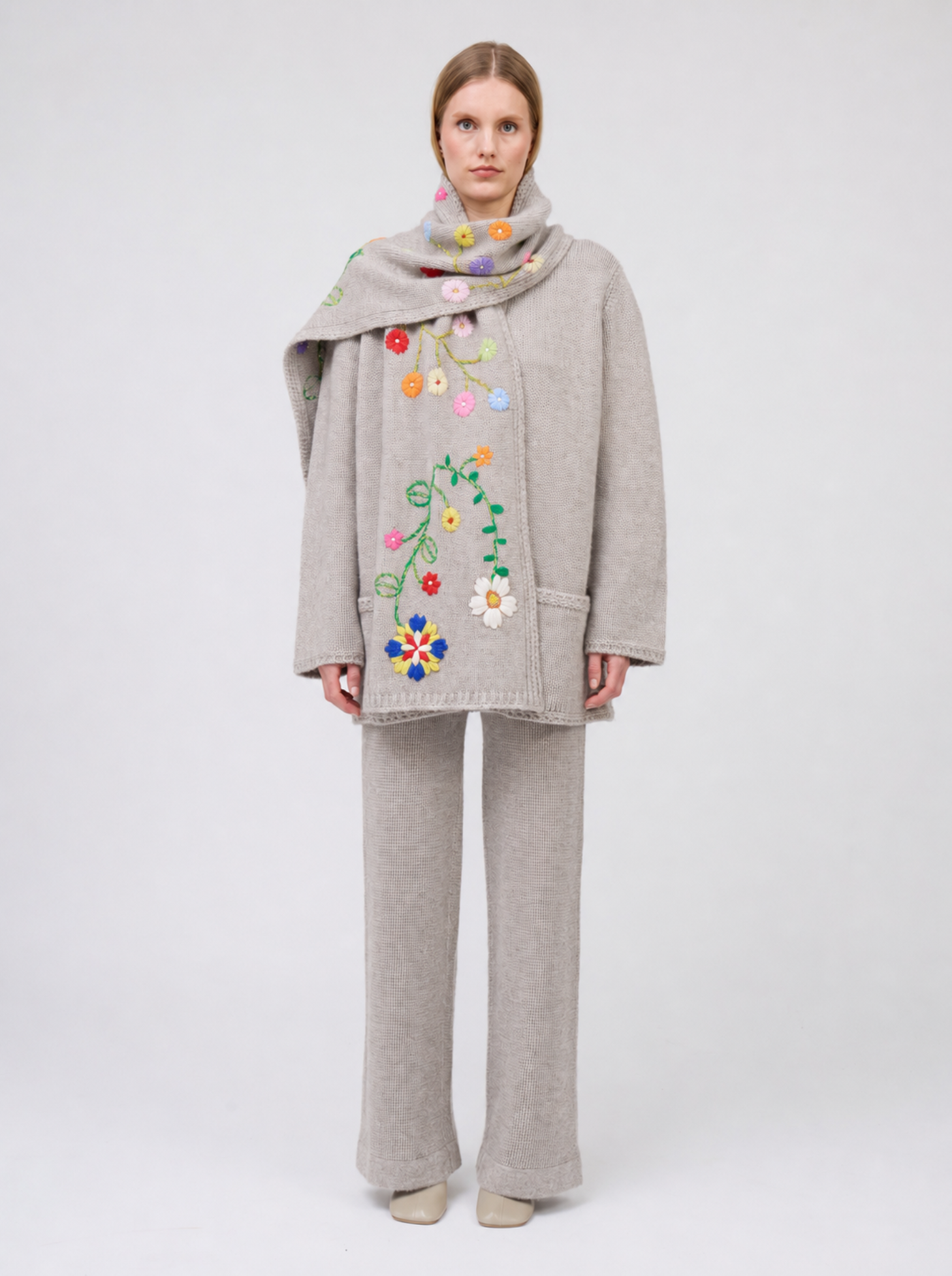 model wears pale beige knitted jacket with flower embroidered scarf and matching pants.