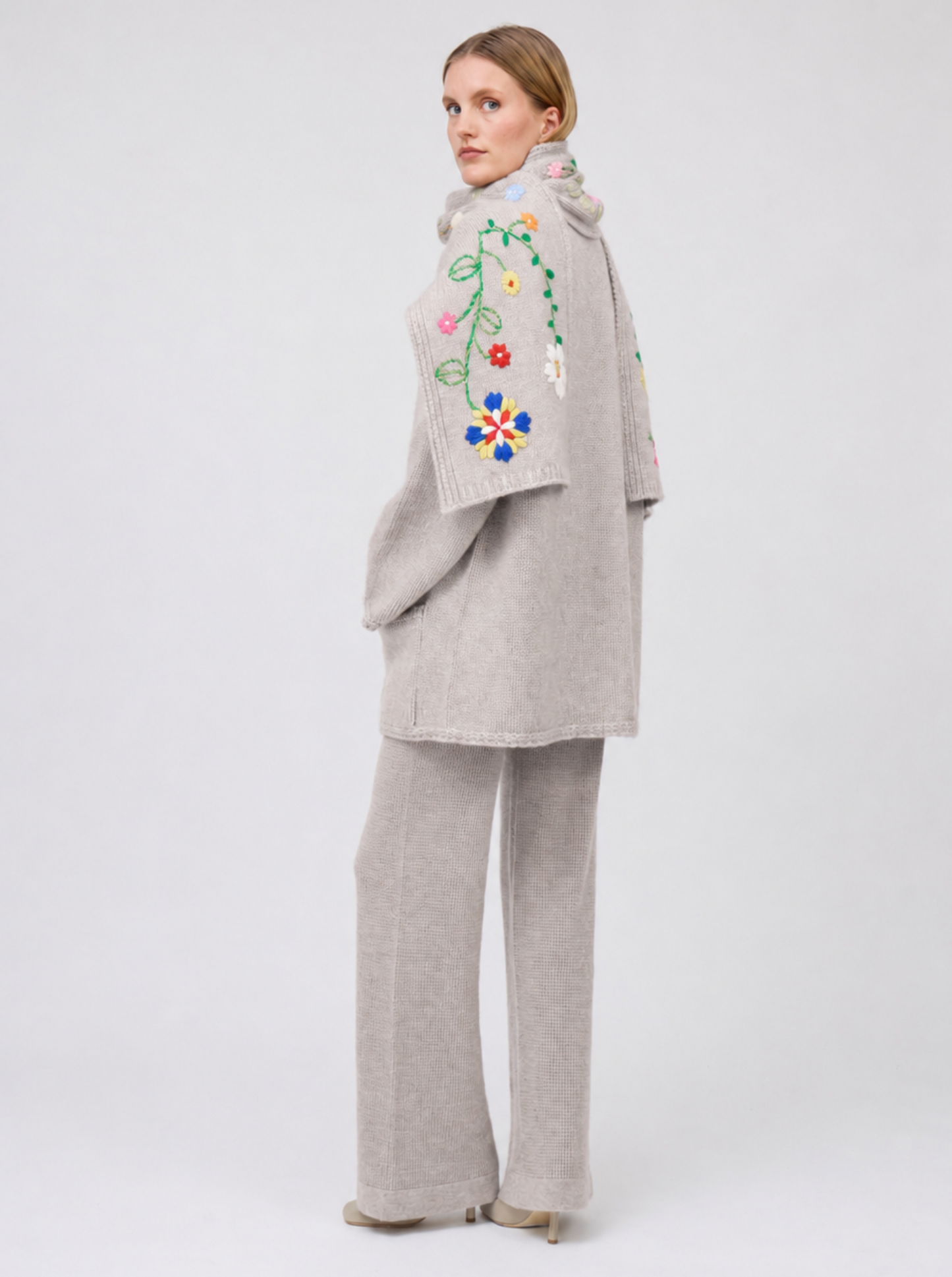 side view model in pale beige knitted jacket with flower embroidered scarf and matching cashmere knit pants.