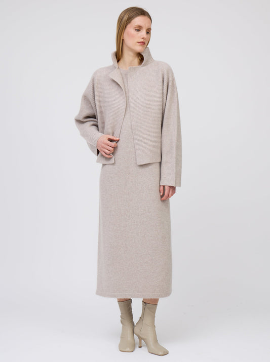 Model wears short beige ribbed knit cashmere high collar jacket over matching beige cashmere straight cut dress and beige boots.