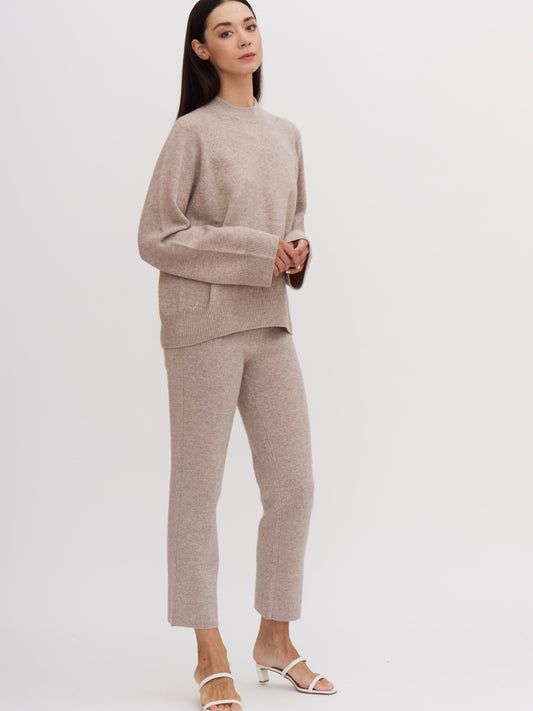 Model wearing beige cashmere outfit: cashmere mock neck jumper with wide sleeves with matching cropped suit pants.