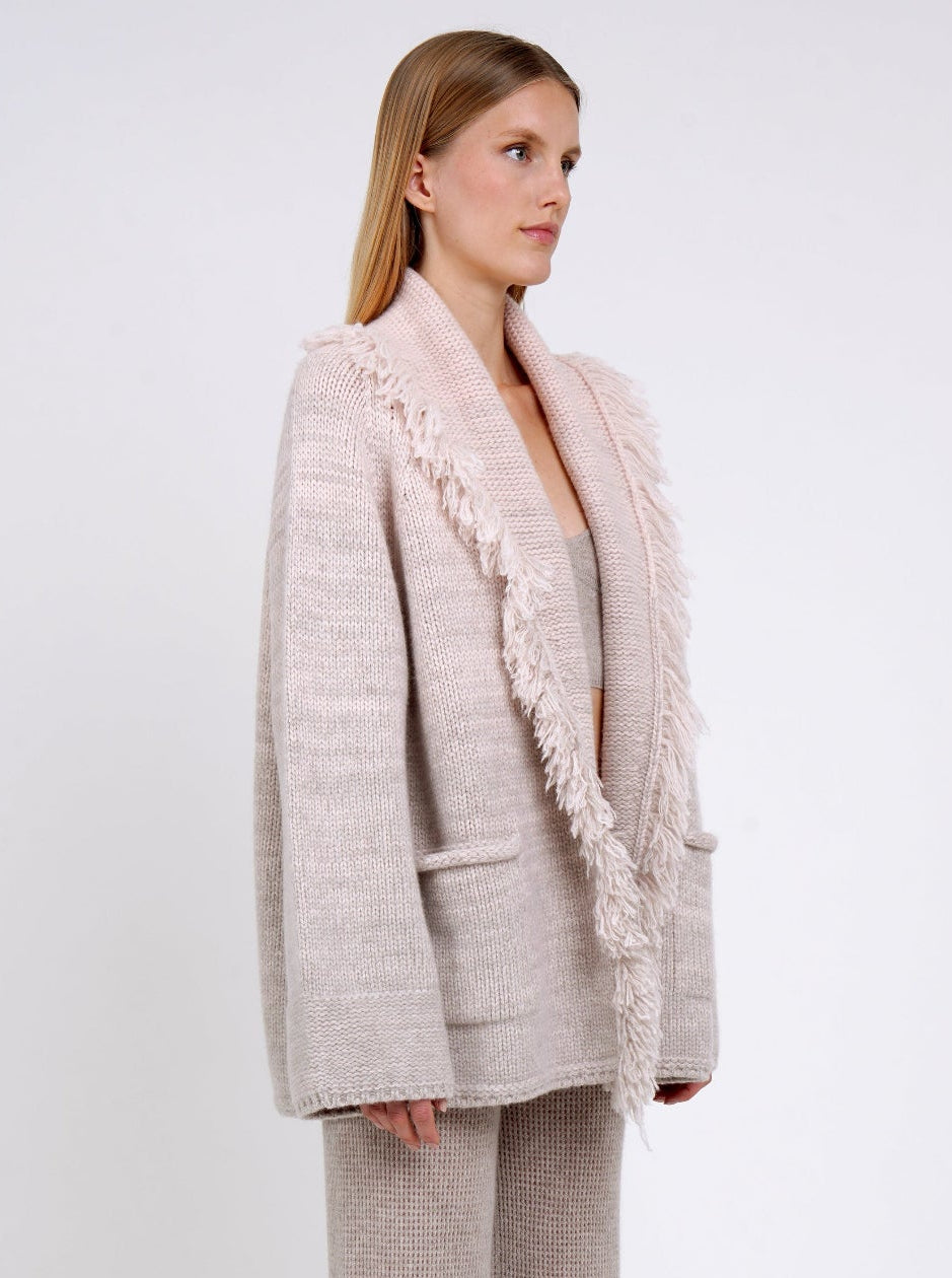 side view model in chunky knit cashmere jacket with fringed shawl collar in beige and pastel peach colours with and beige knit pants.