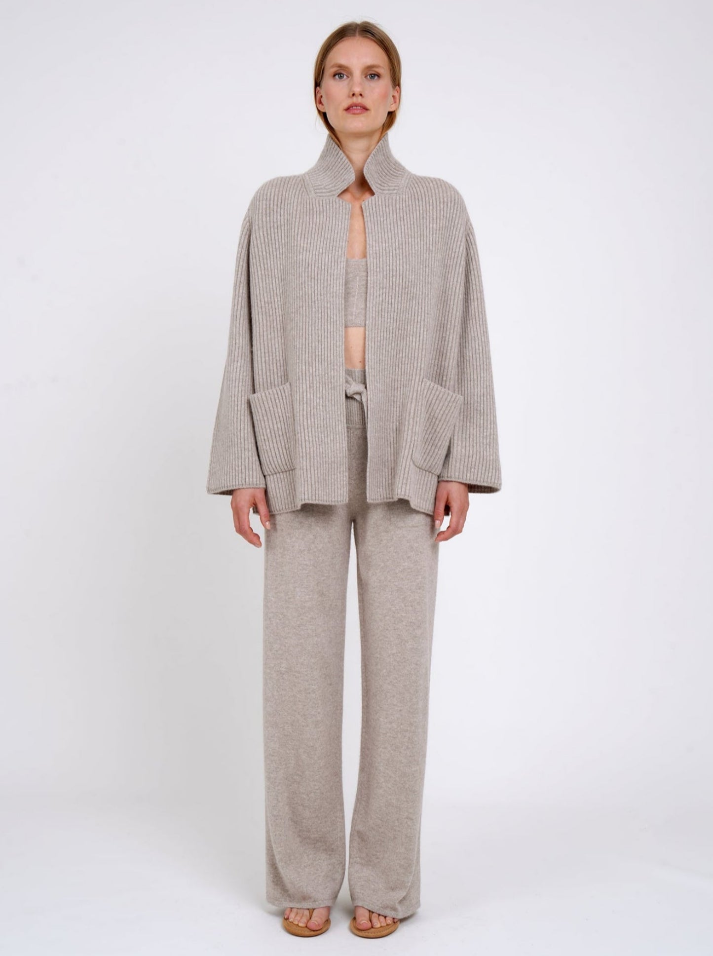 Front view model wearing beige ribbed knit cashmere jacket with high collar and patch pockets; worn with beige cashmere top and pants.