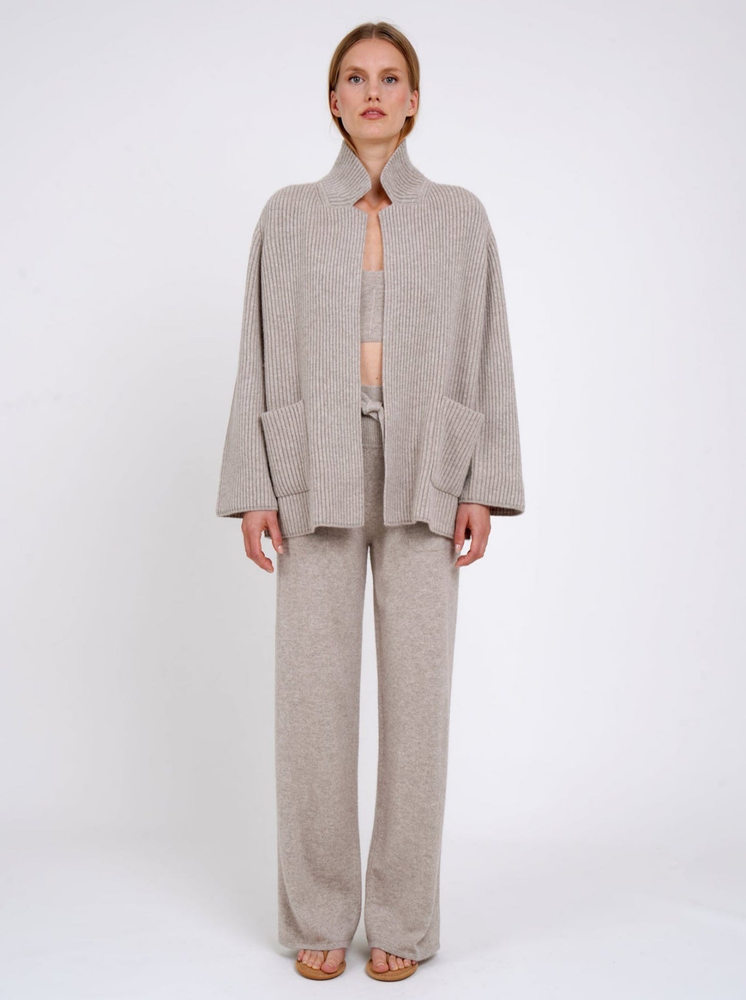 Front view model wearing beige ribbed knit cashmere jacket with high collar and patch pockets; worn with beige cashmere top and pants.