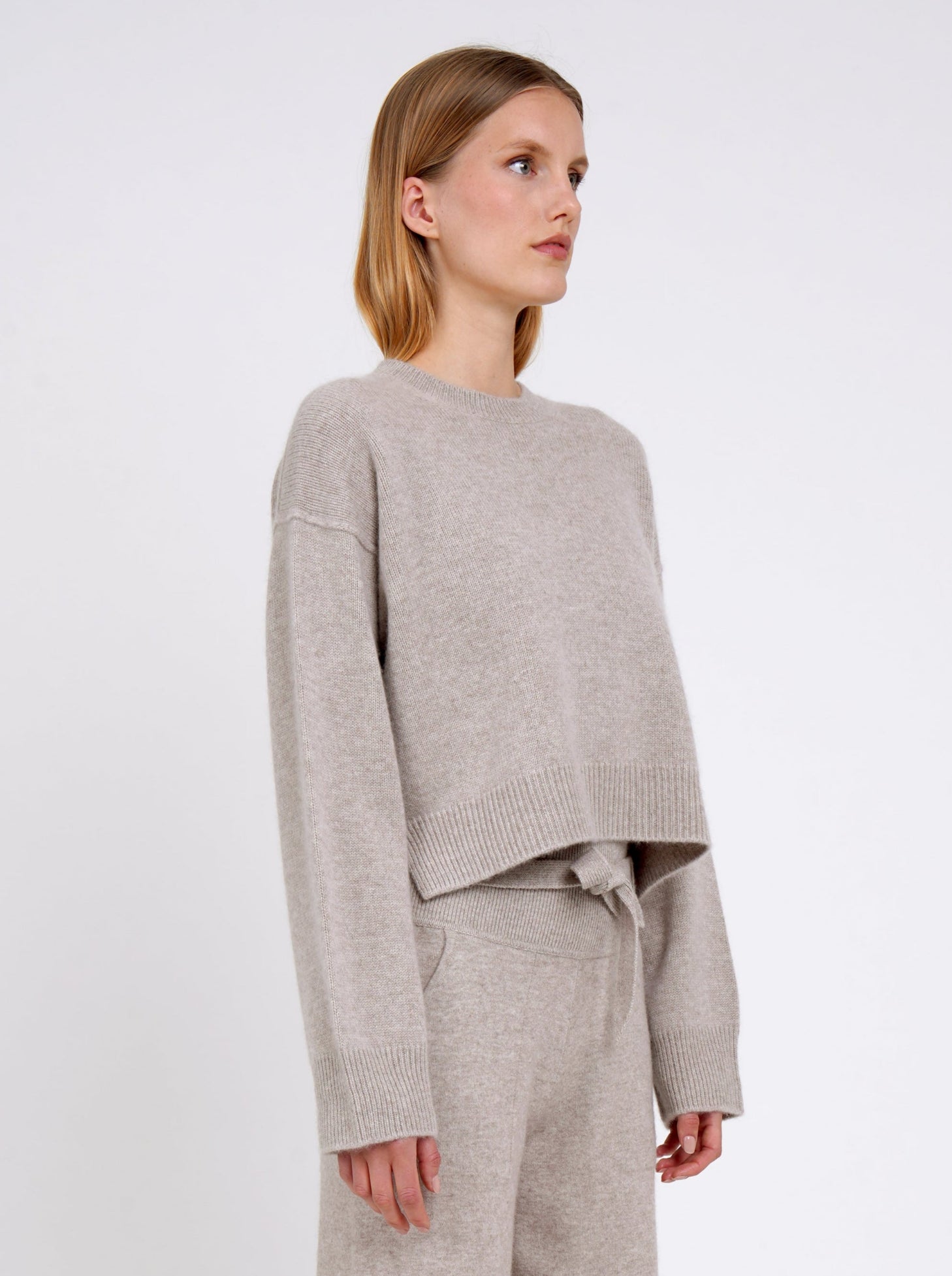 Close up side view model wearing beige cashmere cropped jumper with round neck, long sleeves.