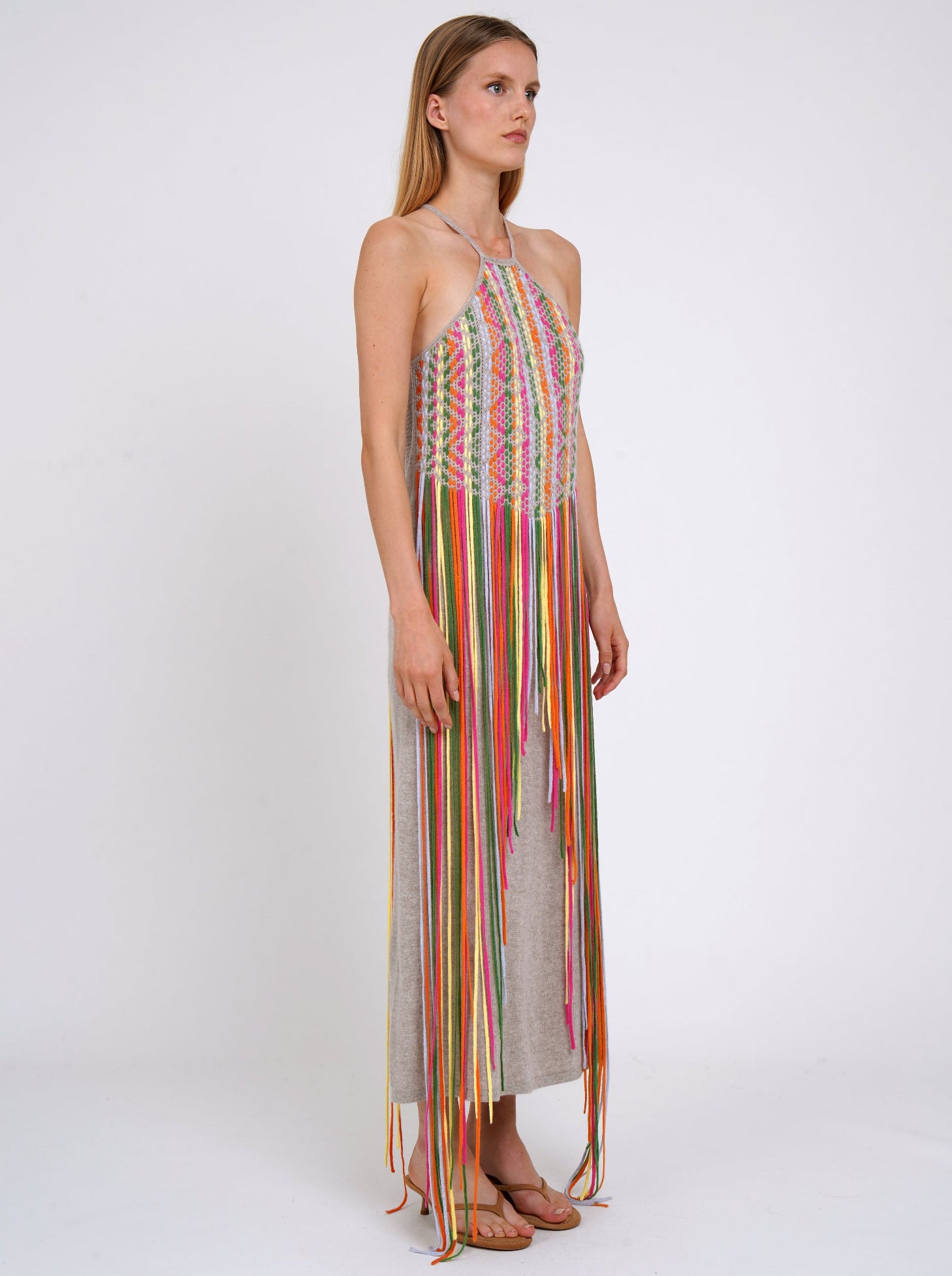 side view of light weight cashmere shift dress with thin halterneck straps and decorated with coloured fringes which flow to the ground.