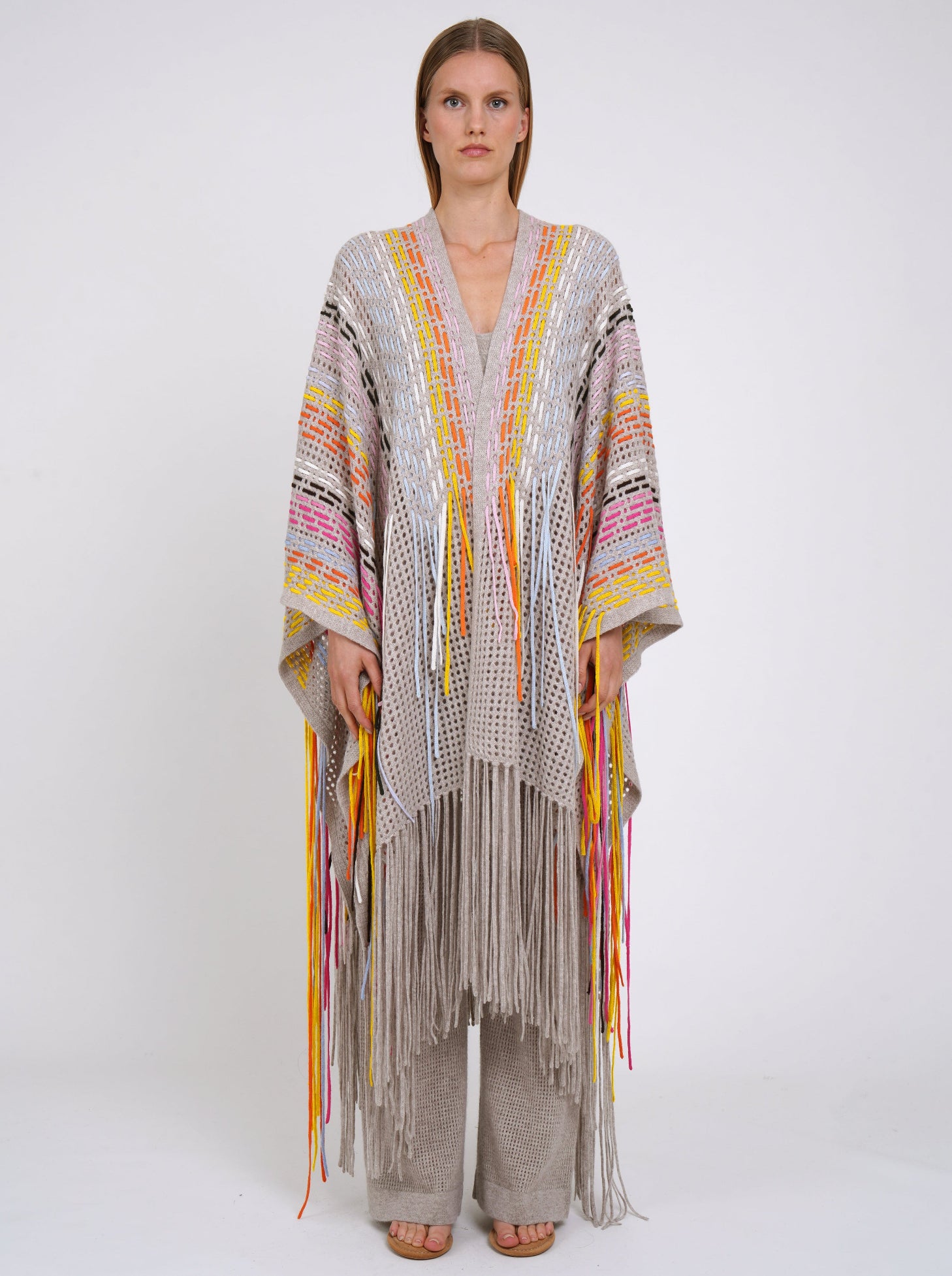 Front view long beige shawl decorated with hand woven multi-colour fringes and matching beige cashmere knit pants.