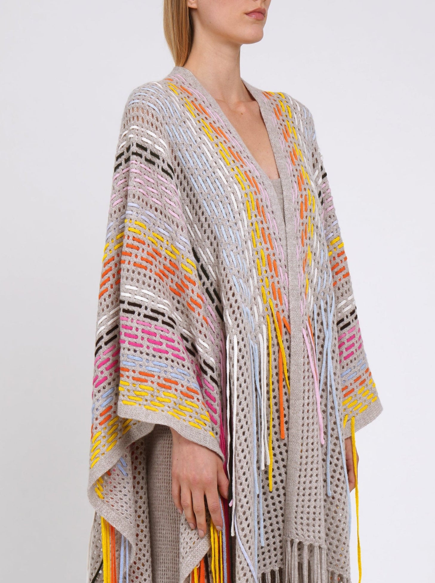 cropped side view detail shows long beige cashmere shawl decorated with hand woven multi-colour fringes.