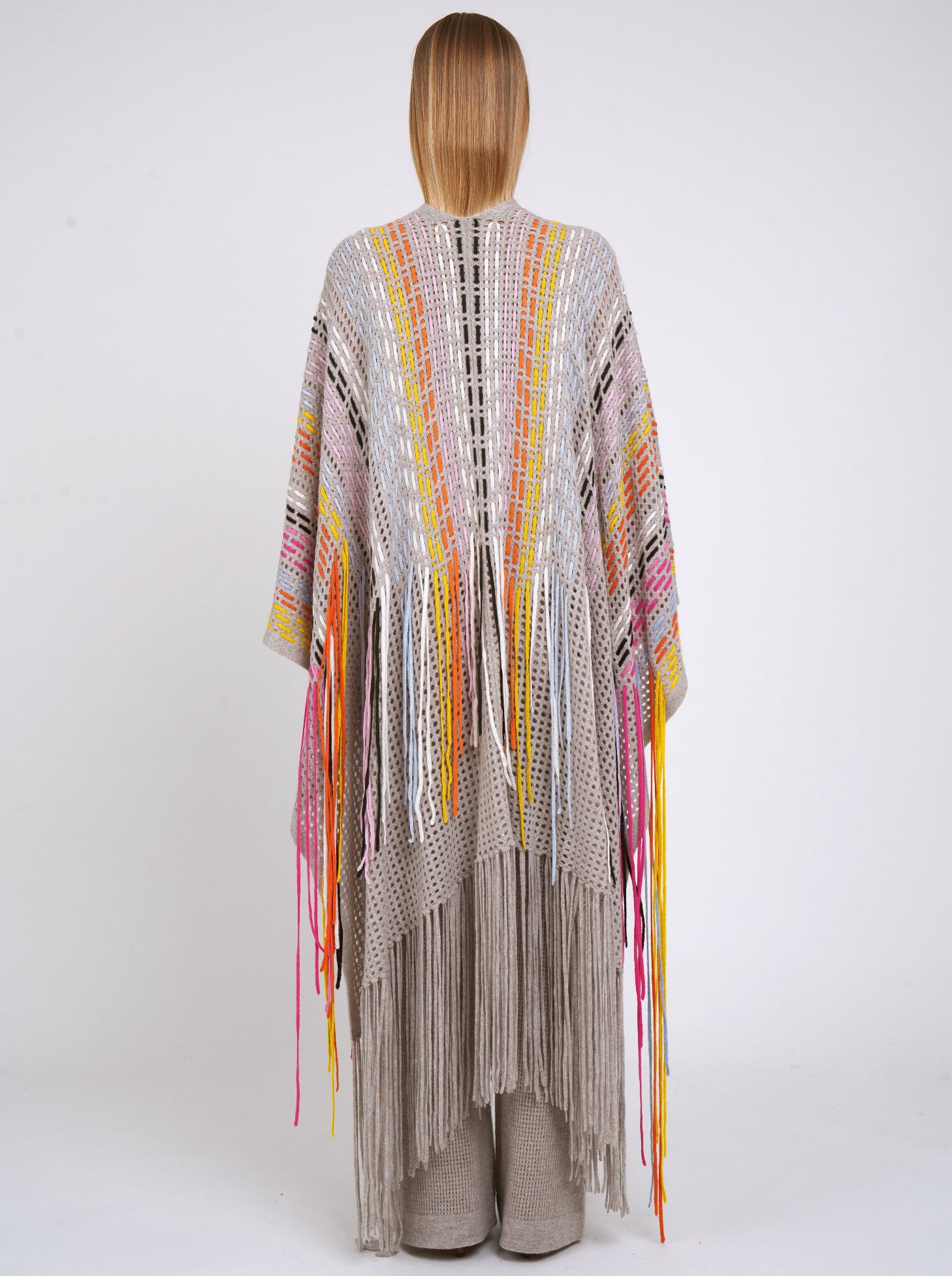 Back view long beige shawl decorated with hand woven multi-colour fringes and matching beige cashmere knit pants.