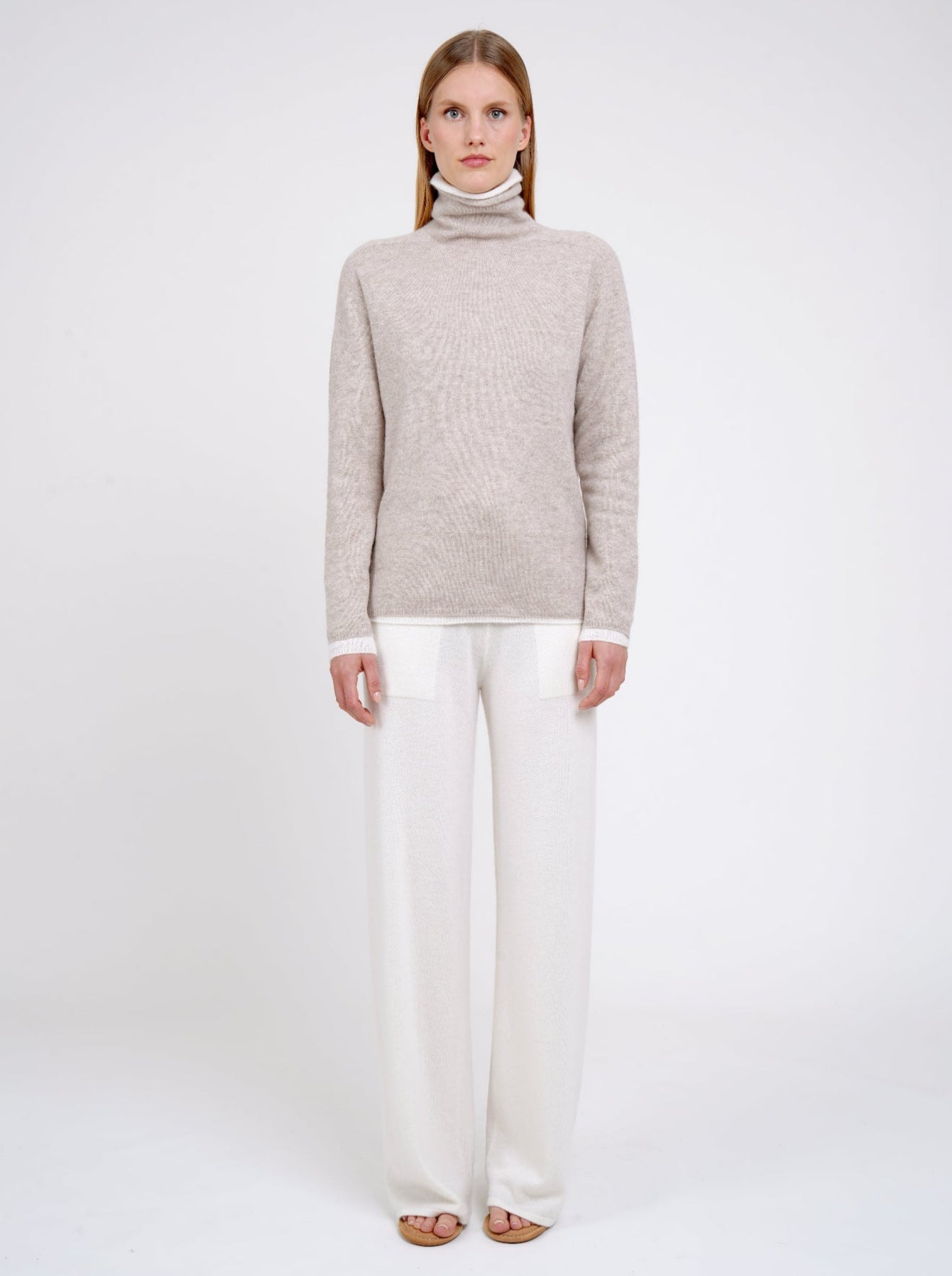 Front view Model wearing double set of white and beige roll neck cashmere jumper with white cashmere wide leg pants.