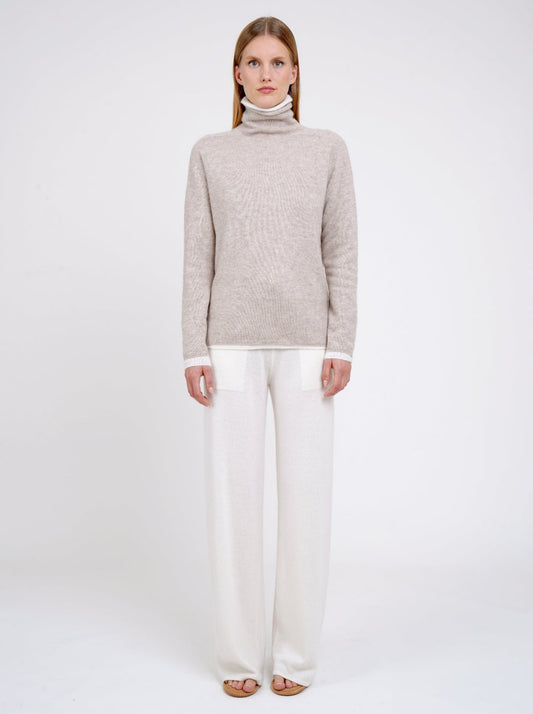 Front view Model wearing double set of white and beige roll neck cashmere jumper with white cashmere wide leg pants.