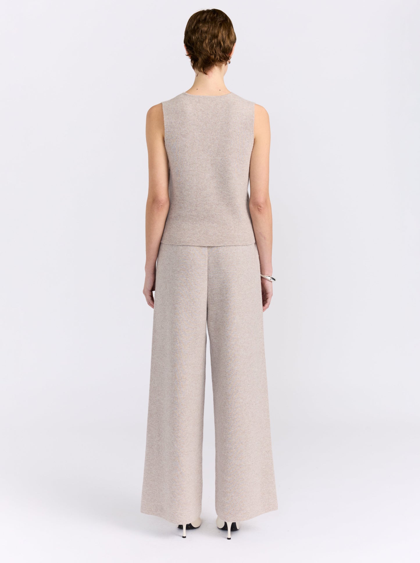 A model shown from the back wearing a light beige knit sleeveless top and matching wide-leg trousers, photographed against a clean white studio background.