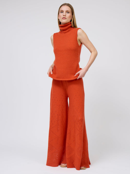 Front view model wears bright orange sleeveless chunky cashmere knit roll neck jumper with matching orange pants.