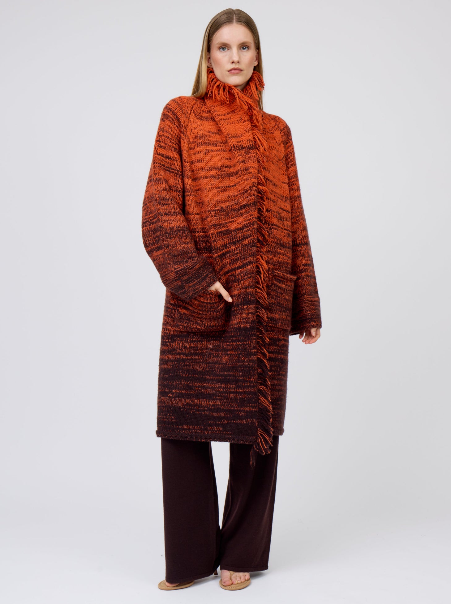 Front view model wearing orange/black mix knit cashmere coat with fringed collar turned up; worn with brown pants.