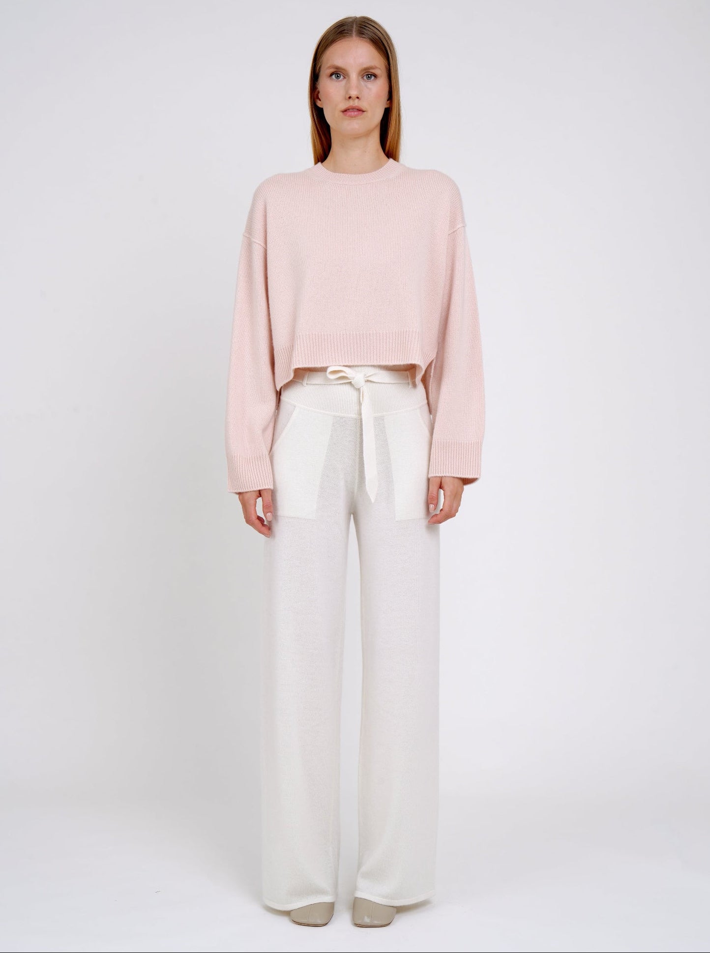 Model wearing a light pink sweater and white pants on a plain background