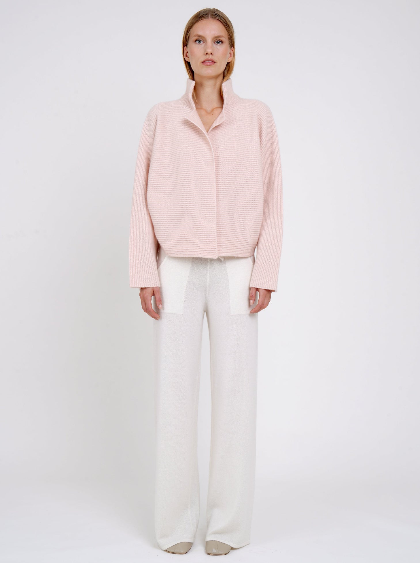 Front view modal in ribbed knit peach cashmere short jacket with high collar kimono sleeves and white wide leg knit pants.