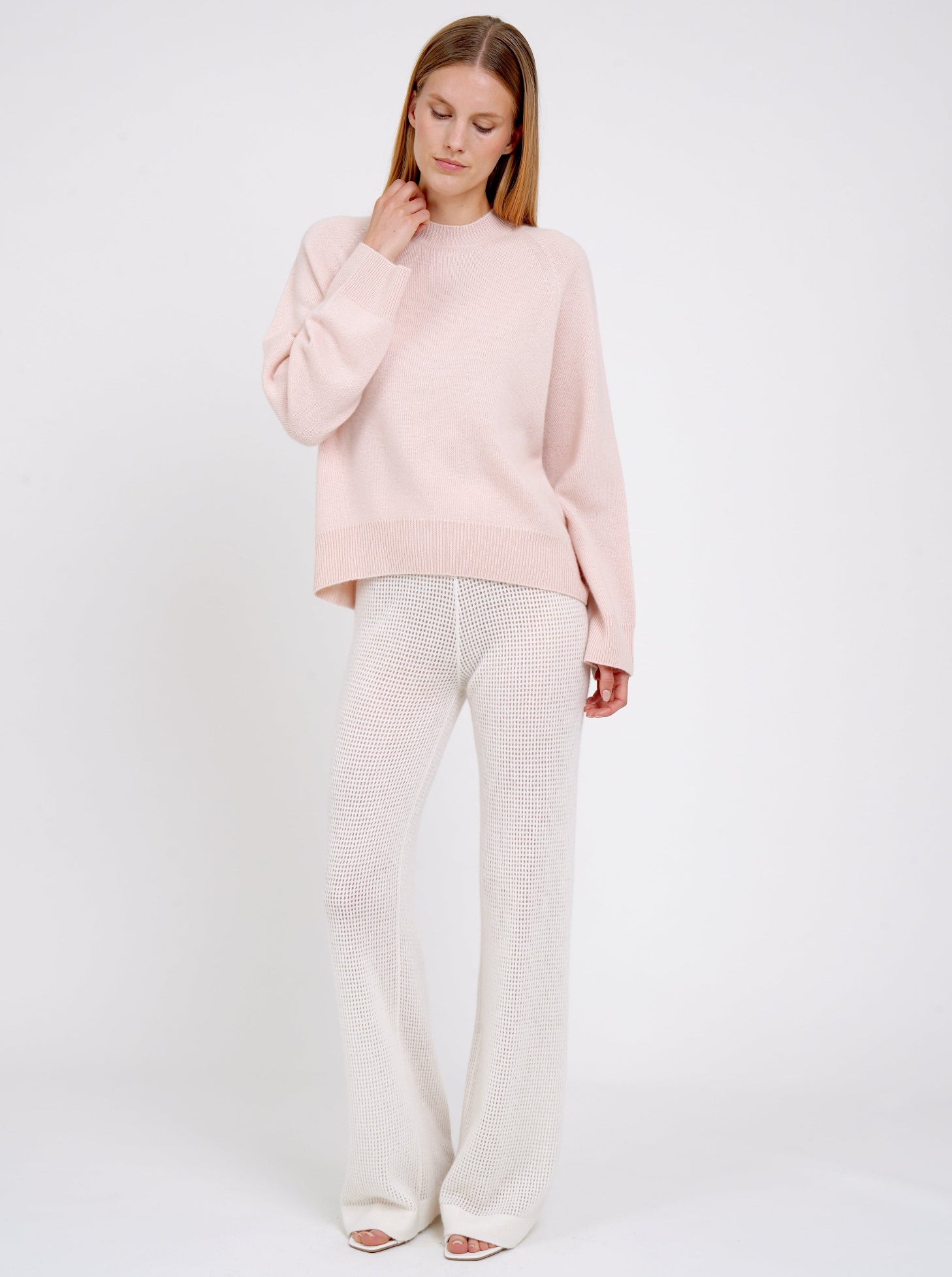 Model wears peach cashmere jumper with round neck, long sleeves and white net knit cashmere pants.