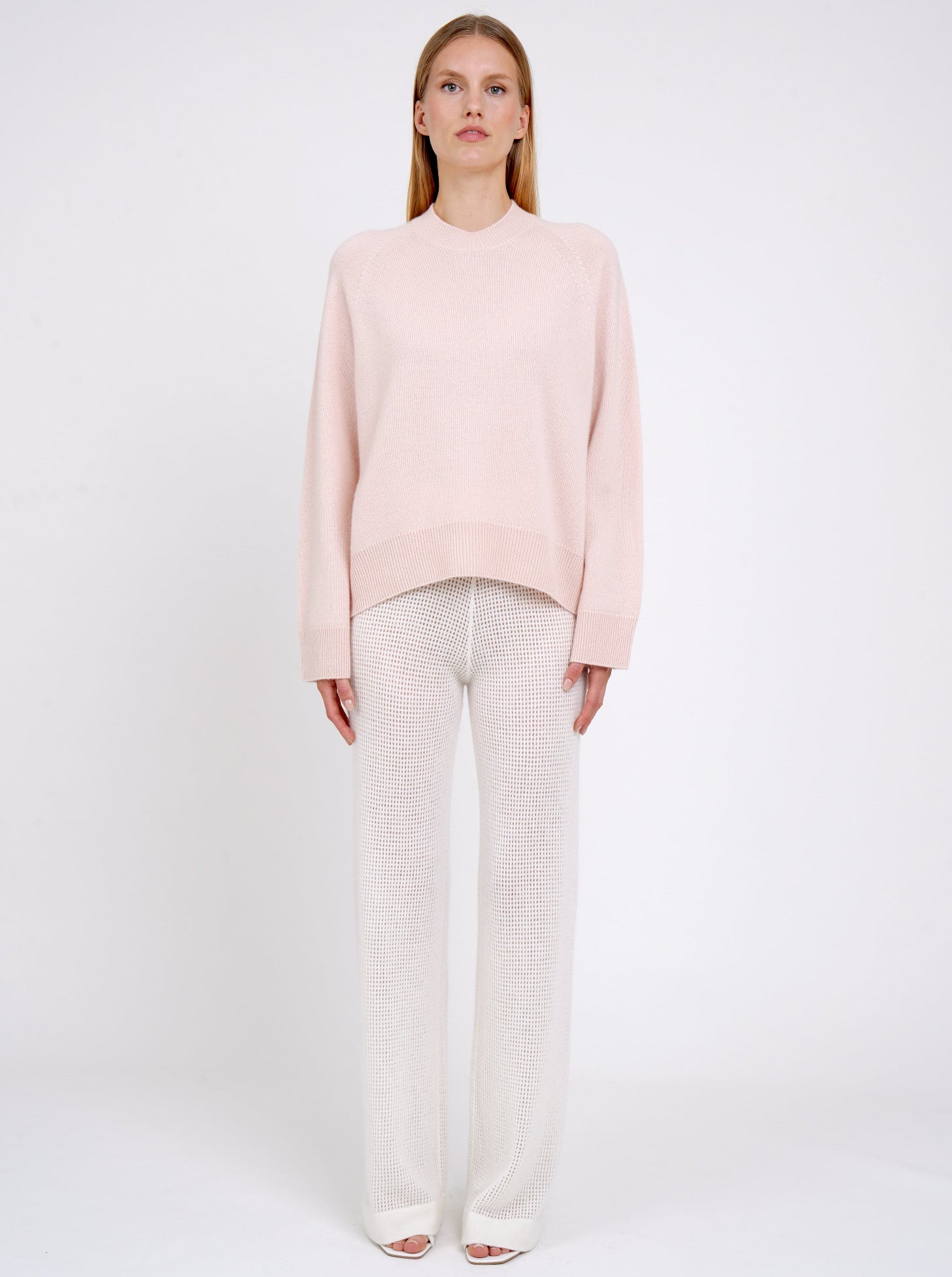 Front view model in peach cashmere jumper with round neck, long sleeves and white net knit wide leg pants.