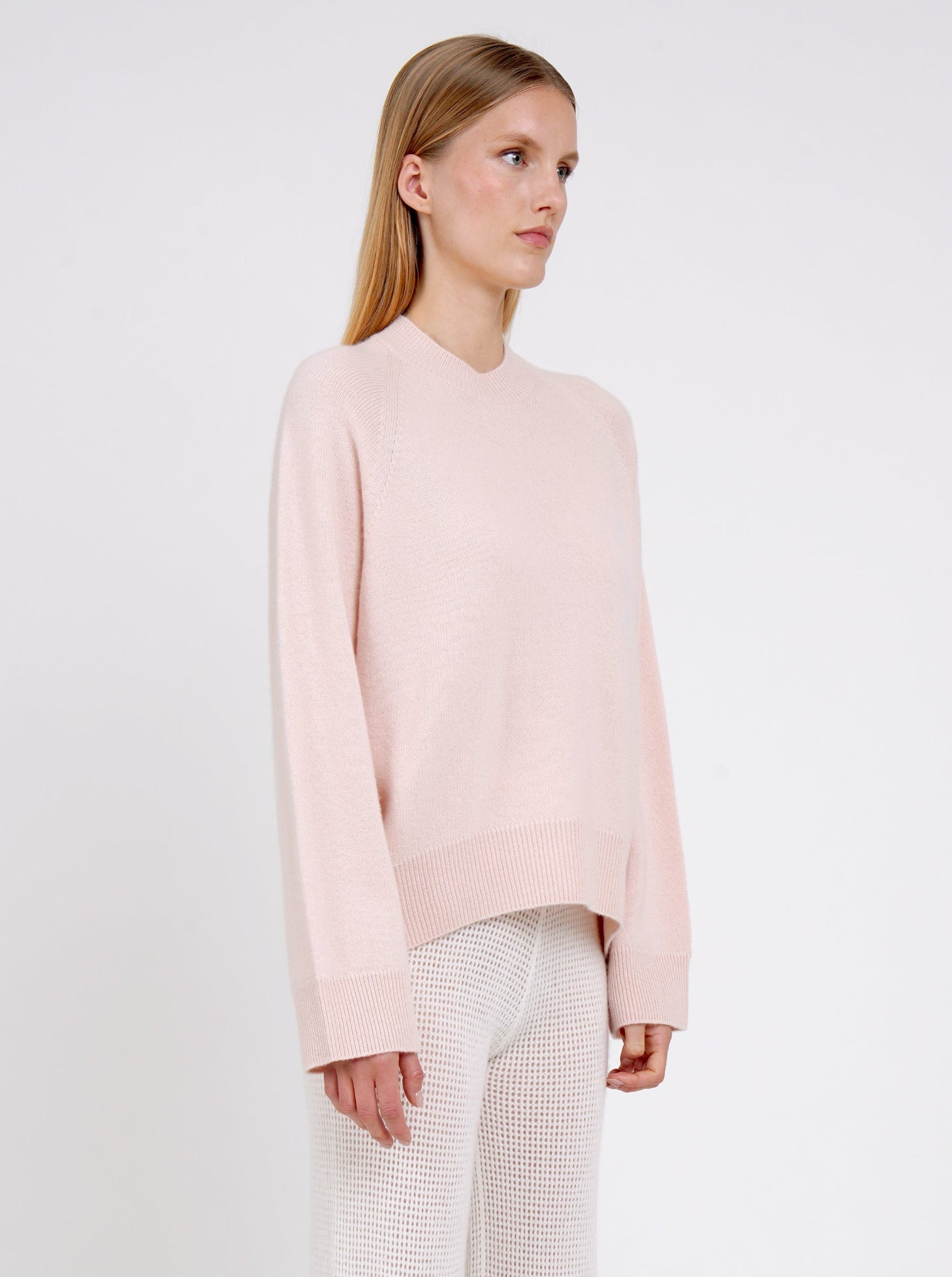 Close up in peach cashmere jumper with round neck, long sleeves and white pants.