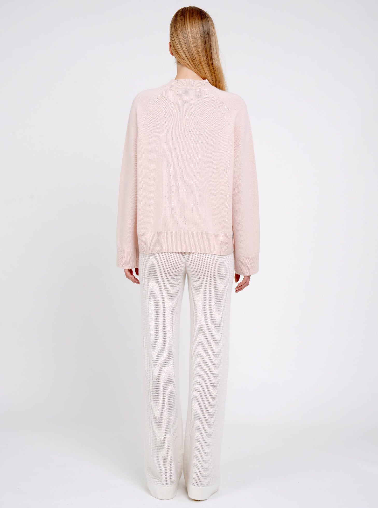 Back view model in peach cashmere jumper with round neck, long sleeves and white net knit wide leg pants