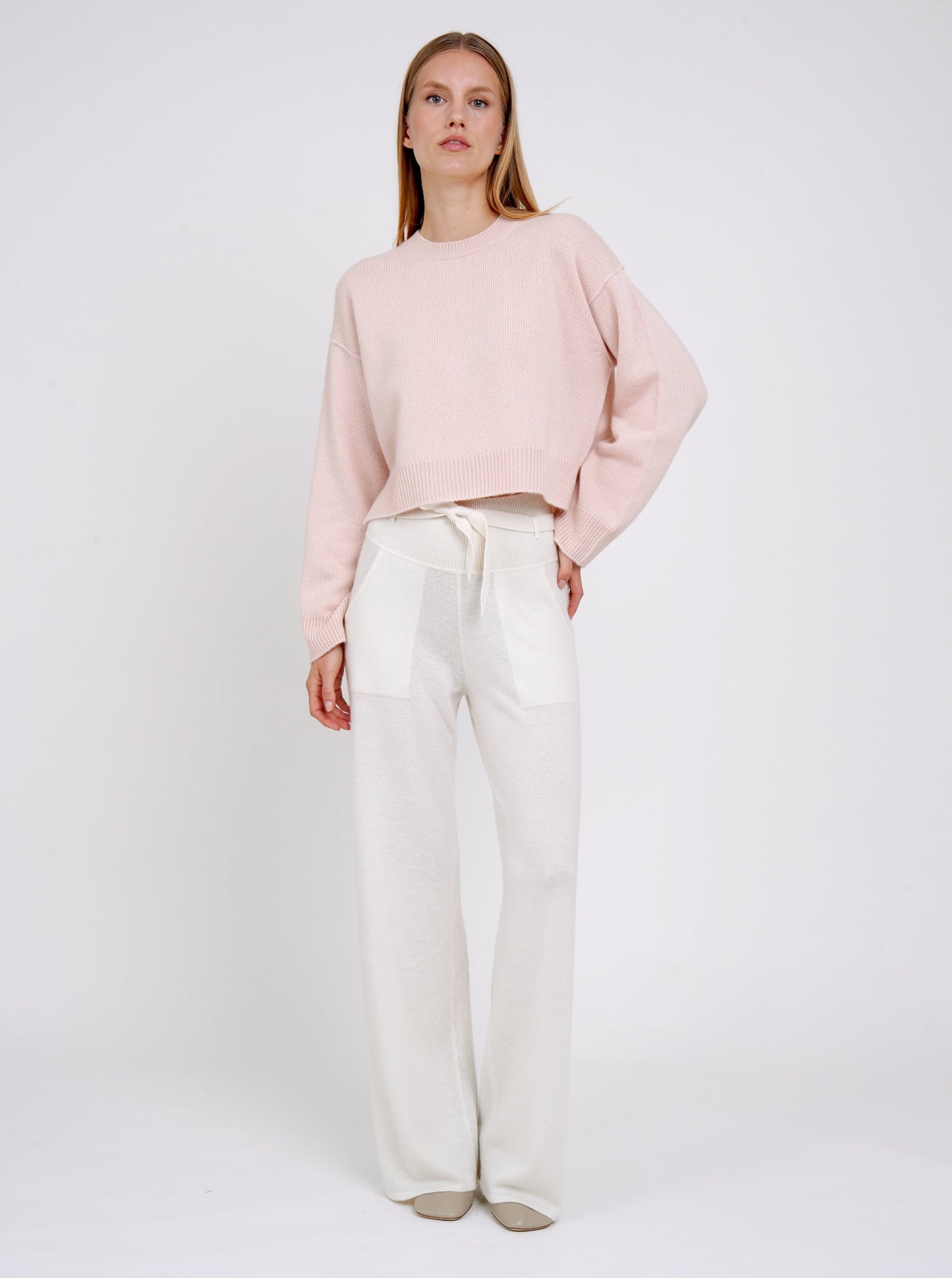 Model wearing a light pink sweater and white pants on a plain background