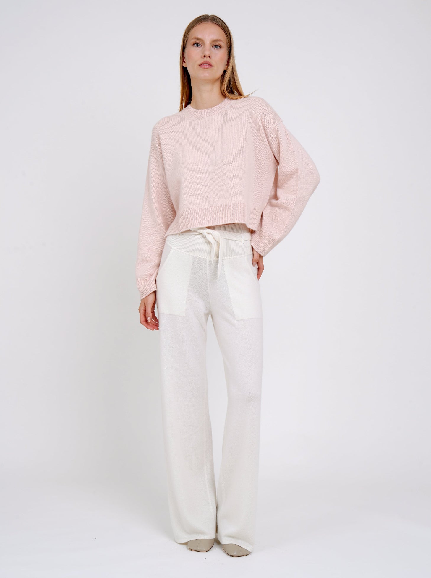Model wearing a light pink sweater and white pants on a plain background