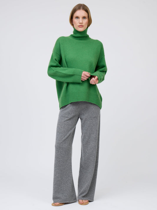Front view, relaxed pose, model wears pine green cashmere roll neck oversized jumper with grey cashmere wide leg pants.