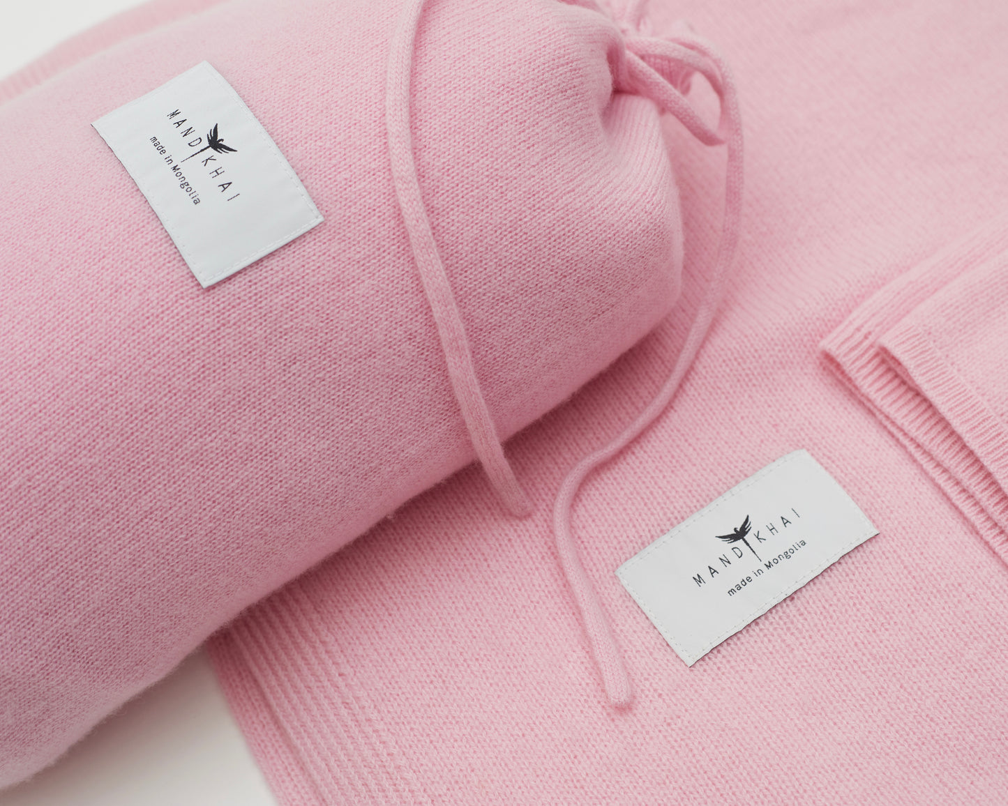 Close up flat lay of the Pink Cashmere Shawl With Travel Pouch featuring Mandkhai's label and the side of the travel pouch 