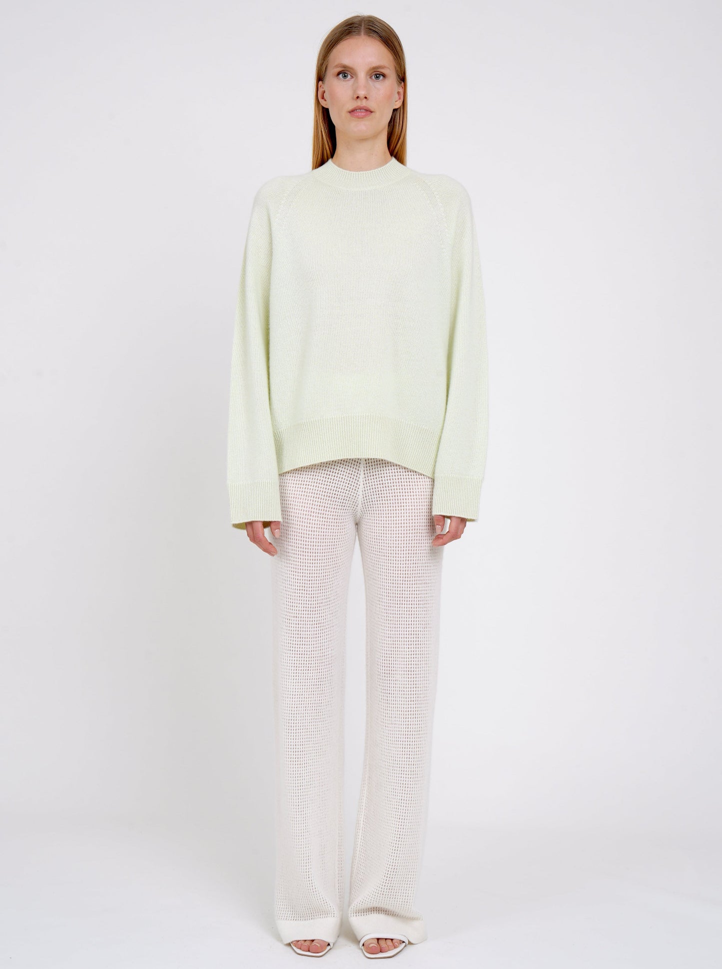 Front view model in pale green cashmere jumper with round neck, long sleeves and white net knit cashmere pants.