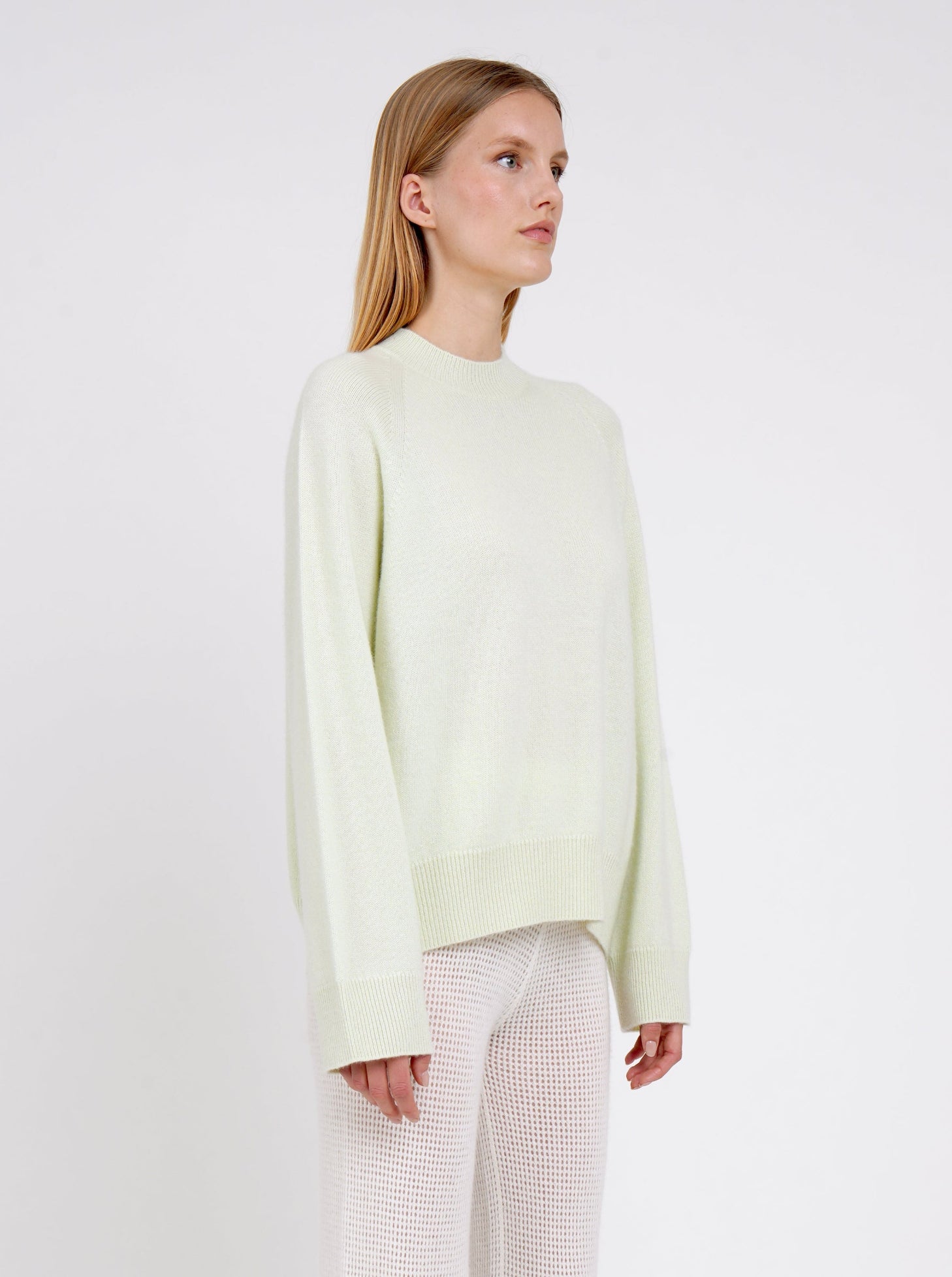Close up model in pale green cashmere jumper with round neck, long sleeves and white net knit cashmere pants.