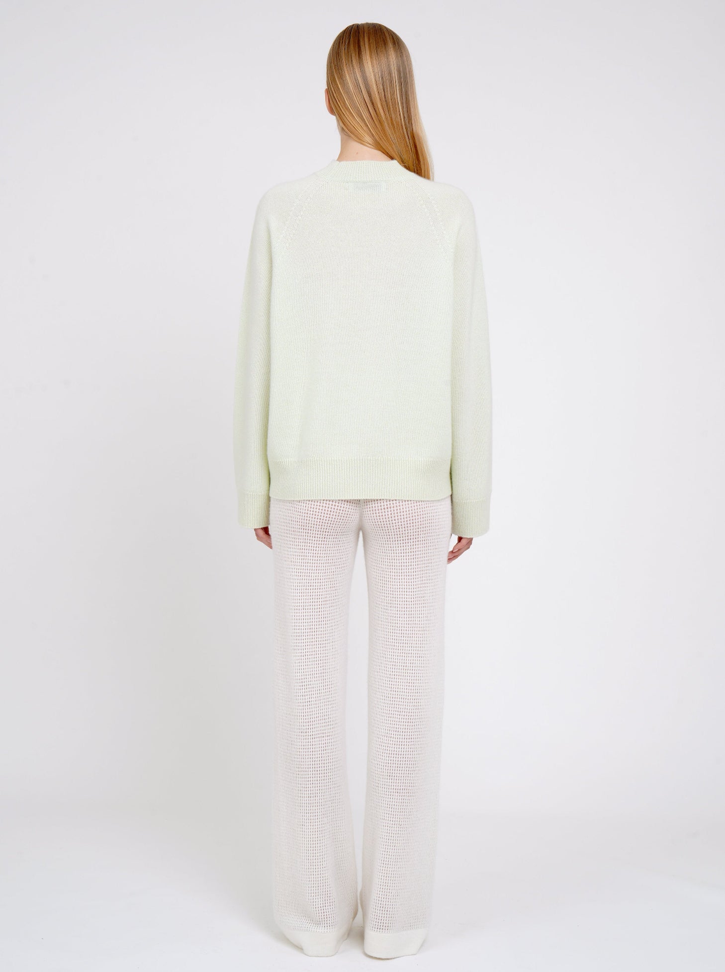 Back view model in pale green cashmere jumper with round neck, long sleeves and white net knit cashmere pants.